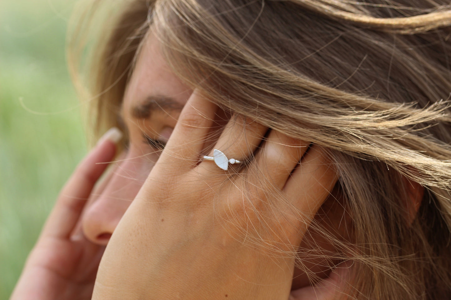Une personne touche ses cheveux en portant la bague Lina | Bague Lait Maternel Argent de Mama Jewels. Larrière-plan flou met en valeur ses cheveux châtain clair et lélégance de cette bague en argent unique.