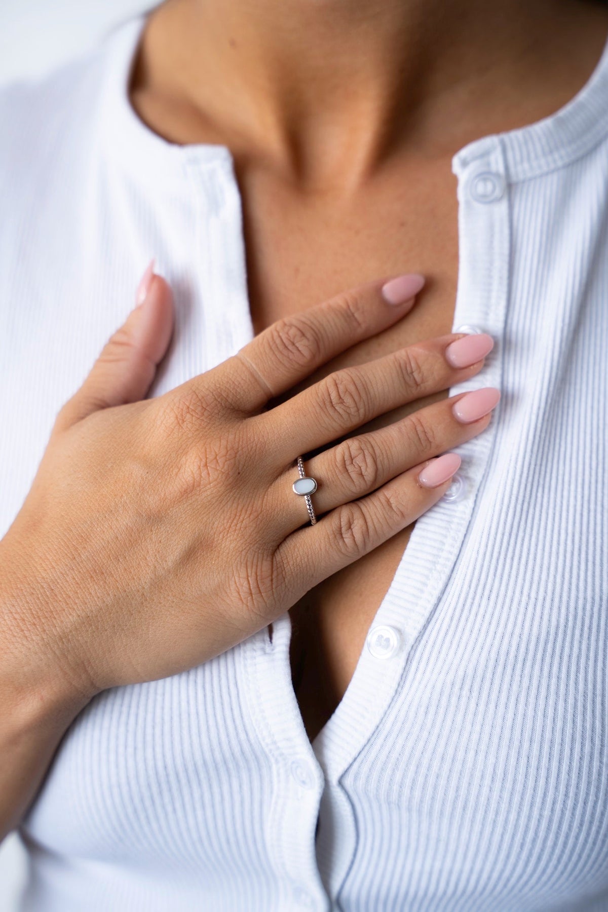 Main sur la poitrine avec la bague au lait maternel Ilse en argent 925, portée avec un gilet côtelé blanc.