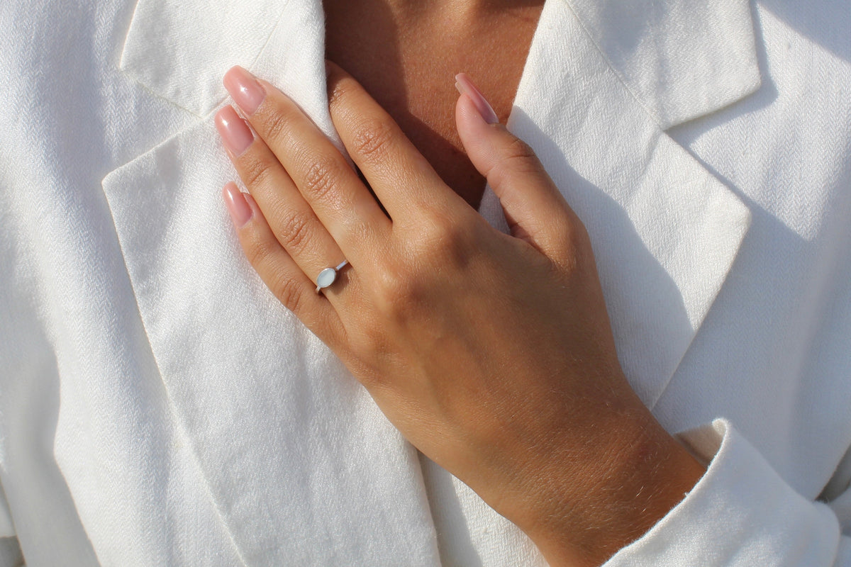 Bague Juna en argent portée, main posée sur la poitrine, veste en lin blanc