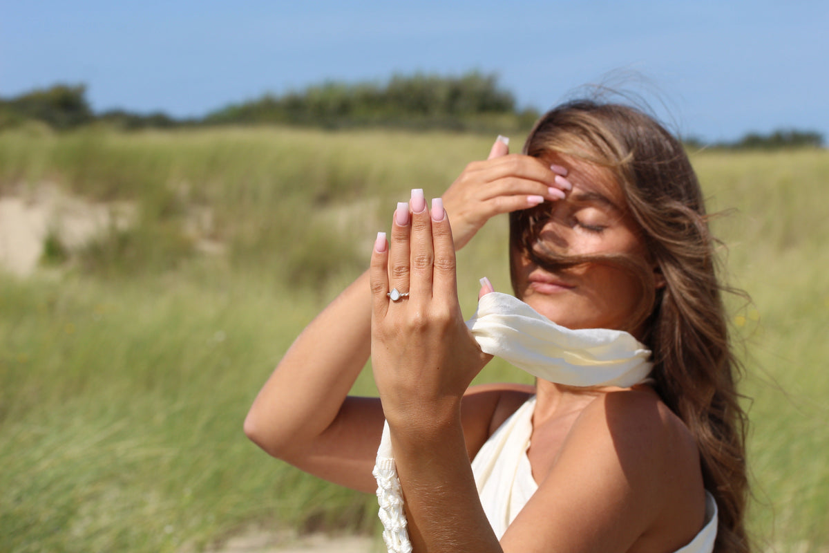 Femme avec foulard blanc dans les dunes, main levée portant la bague Turning Droplet