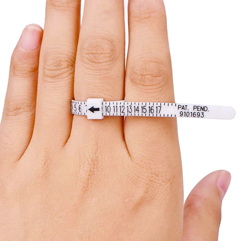 Une main porte la Bague d'ajustement pour une taille de bague parfaite de Mama Jewels, un baguier en plastique blanc avec des marquages numériques clairs et une flèche, s'enroulant autour du doigt pour mesurer facilement la taille de votre bague.