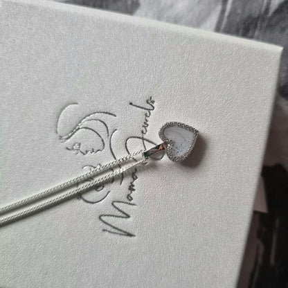 Un pendentif en argent en forme de cœur avec une pierre blanche, connu sous le nom de Demi | Pendentif Lait Maternel Argent de Mama Jewels, est délicatement suspendu à sa chaîne en argent. Il est présenté dans une boîte blanche texturée avec un lettrage script élégant.