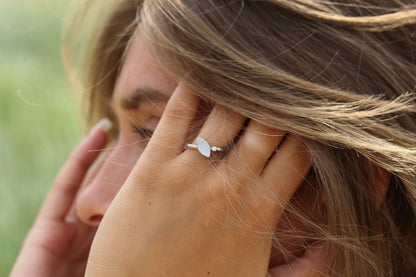Une personne touche ses cheveux en portant la bague Lina | Bague Lait Maternel Argent de Mama Jewels. Larrière-plan flou met en valeur ses cheveux châtain clair et lélégance de cette bague en argent unique.