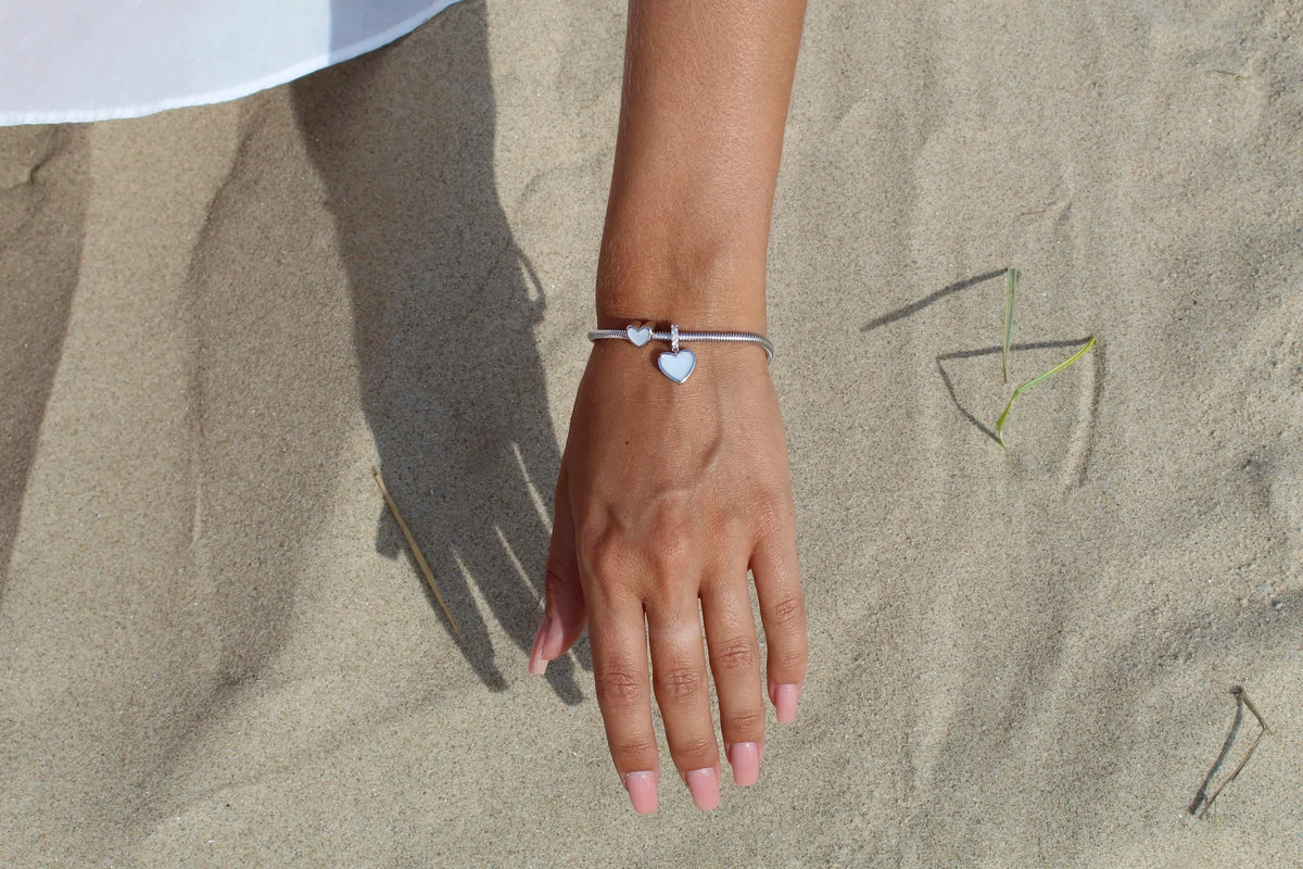 Bracelet à breloques en argent avec pendentif cœur, posé sur le sable