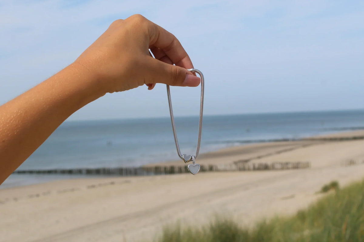 Bracelet à breloques en argent au design sobre, tenu devant une plage
