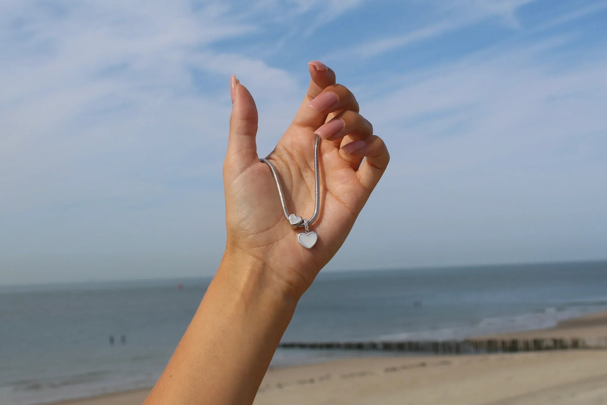 Bracelet à breloques en argent avec pendentif cœur, tenu devant un paysage côtier