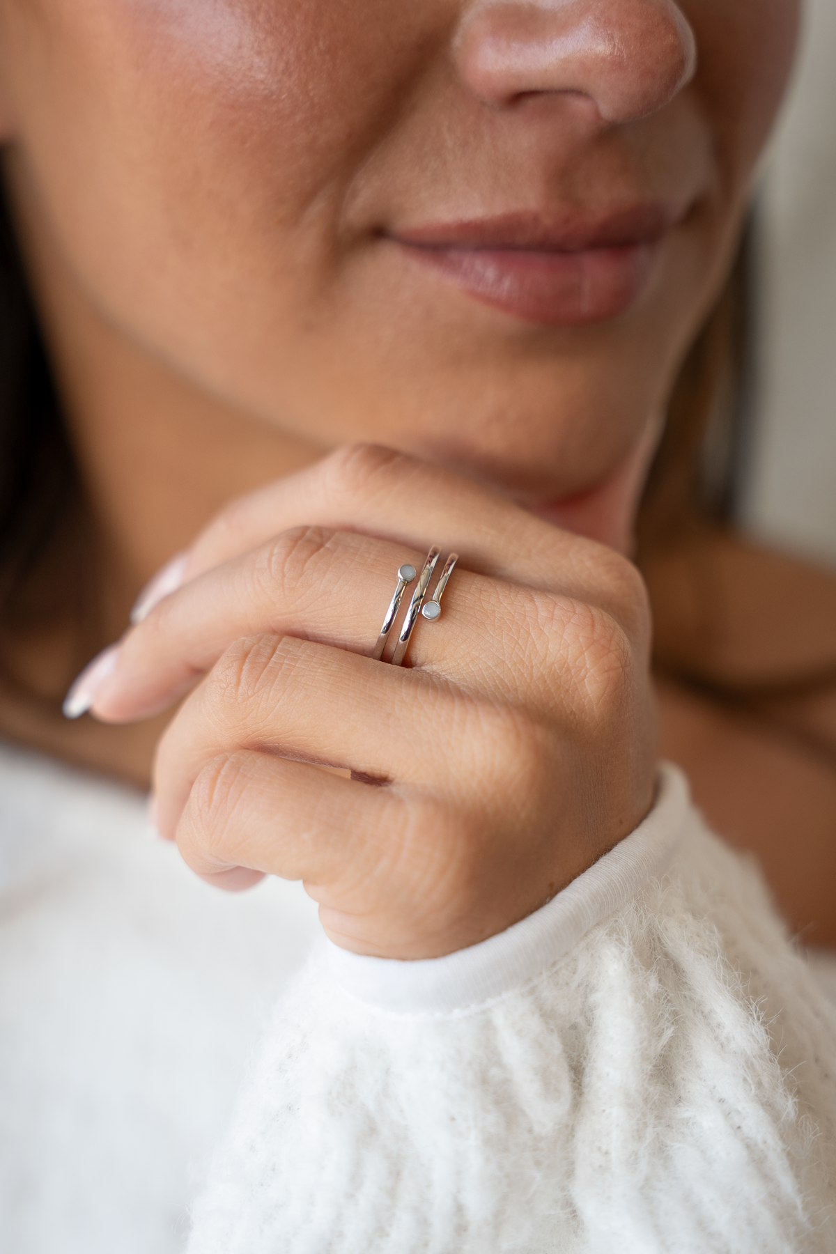 Bague Aurore en argent en spirale portée au doigt, main sous le menton, deux pierres de lait aux extrémités