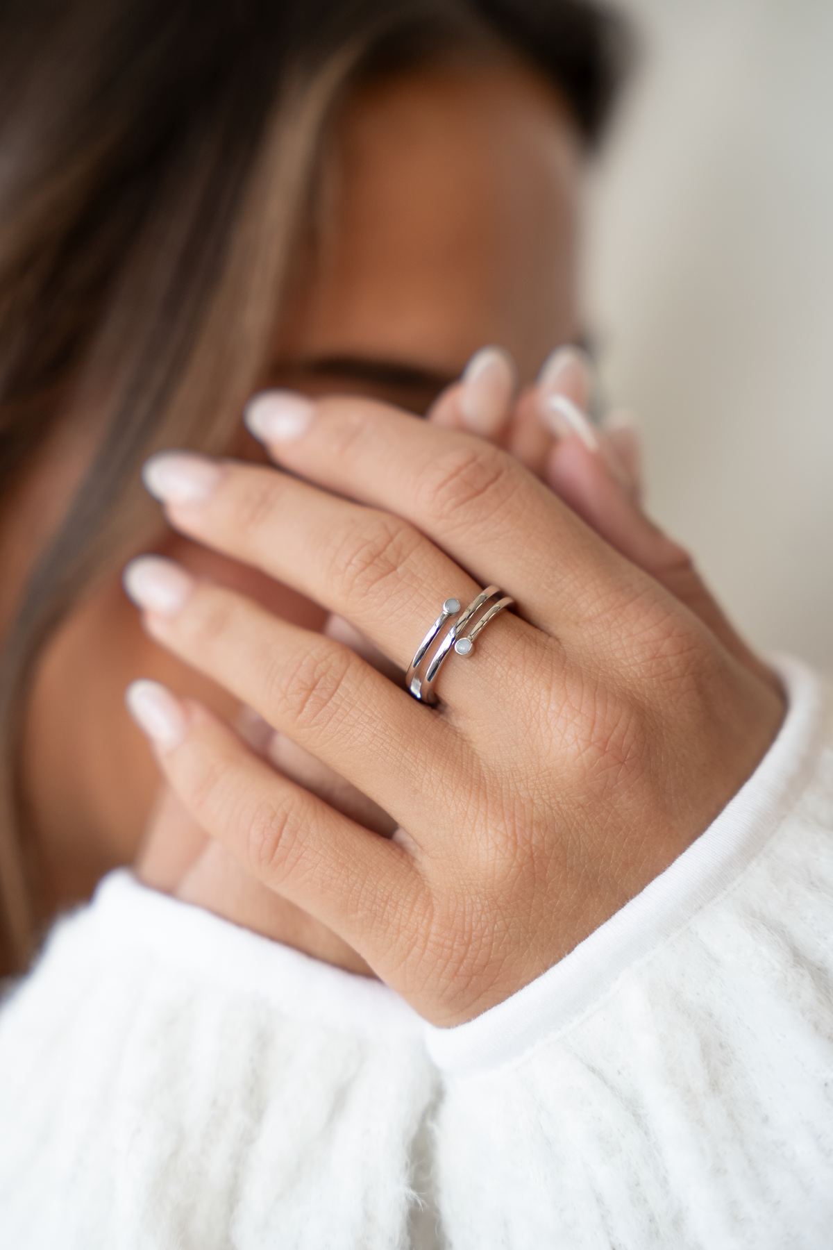 Gros plan d'une main portant la bague Aurore en argent, anneau enroulé avec deux petites pierres de lait