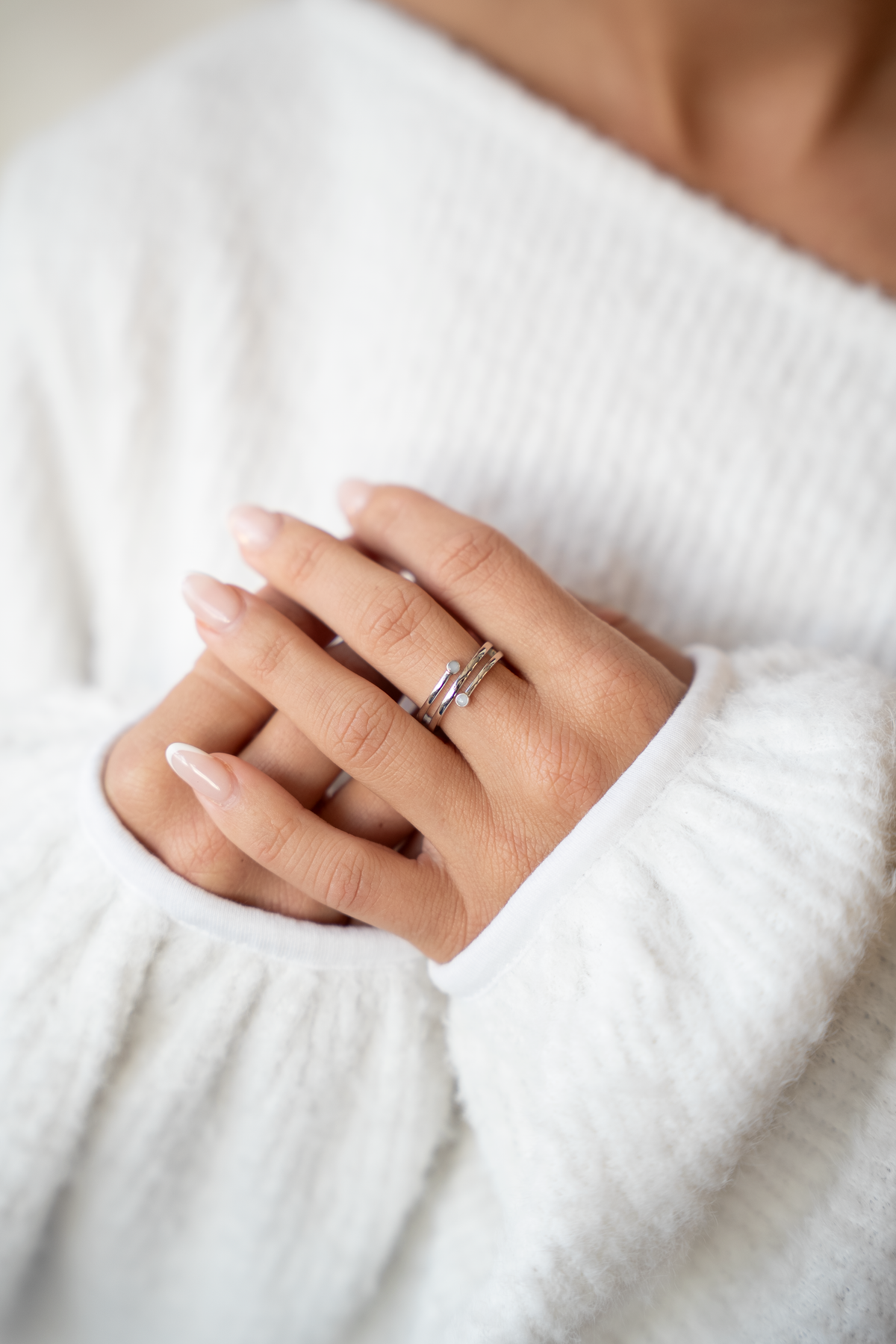 Mains croisées sur un pull blanc, bague Aurore en argent avec deux pierres de lait maternel