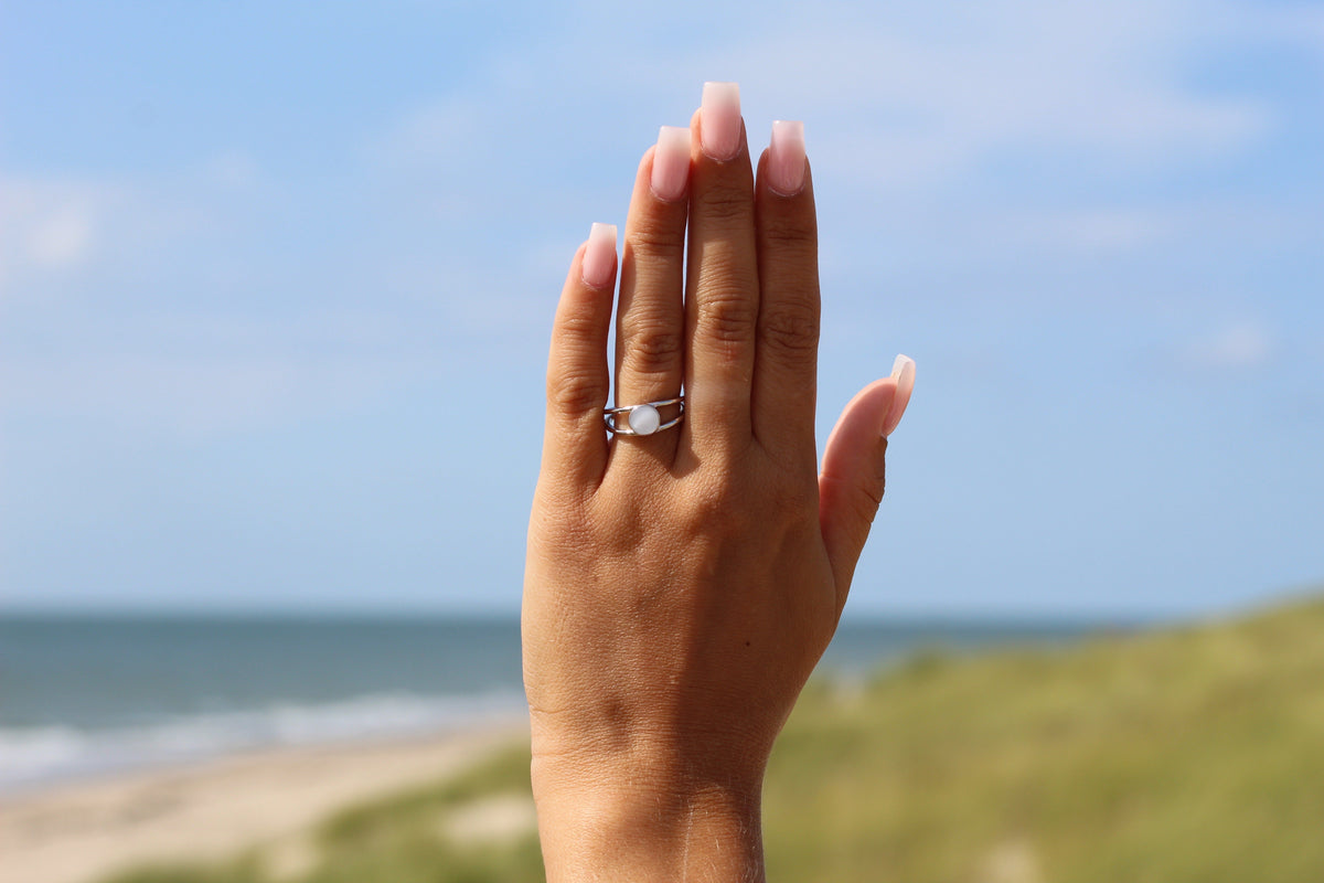 Main levée devant la mer et les dunes avec la bague Bea argentée à deux joncs
