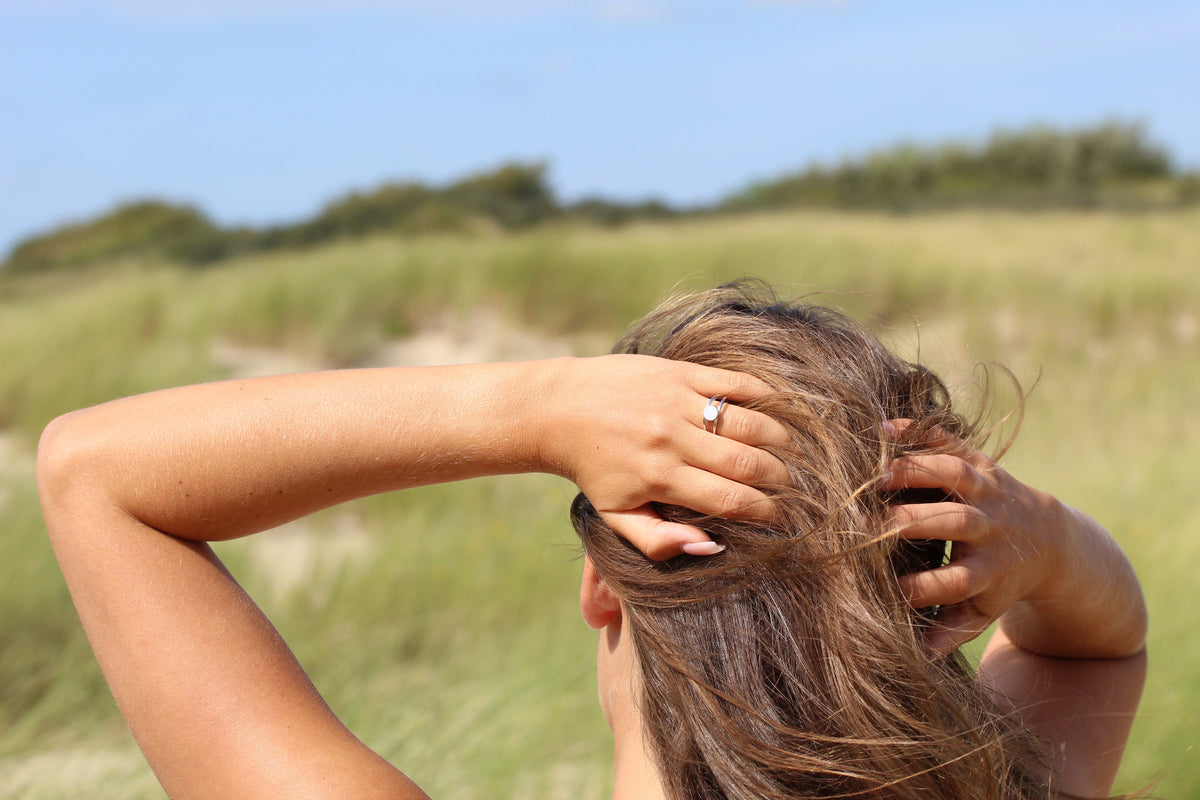 Femme de dos dans les dunes, mains dans les cheveux, portant la bague Bea argentée