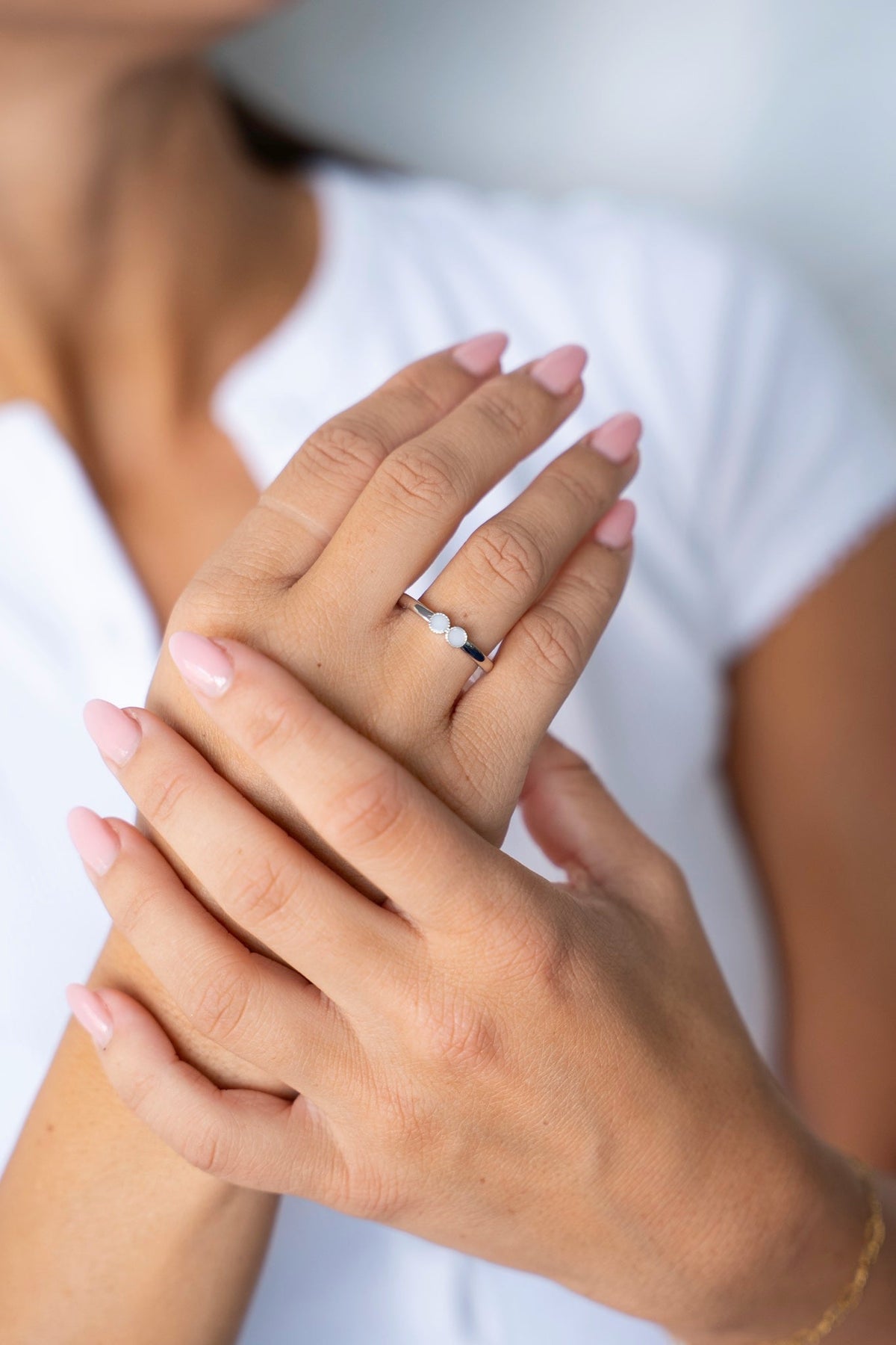 Bague au lait maternel Bo en or blanc massif sur une main posée sur l'autre, devant un t-shirt blanc.