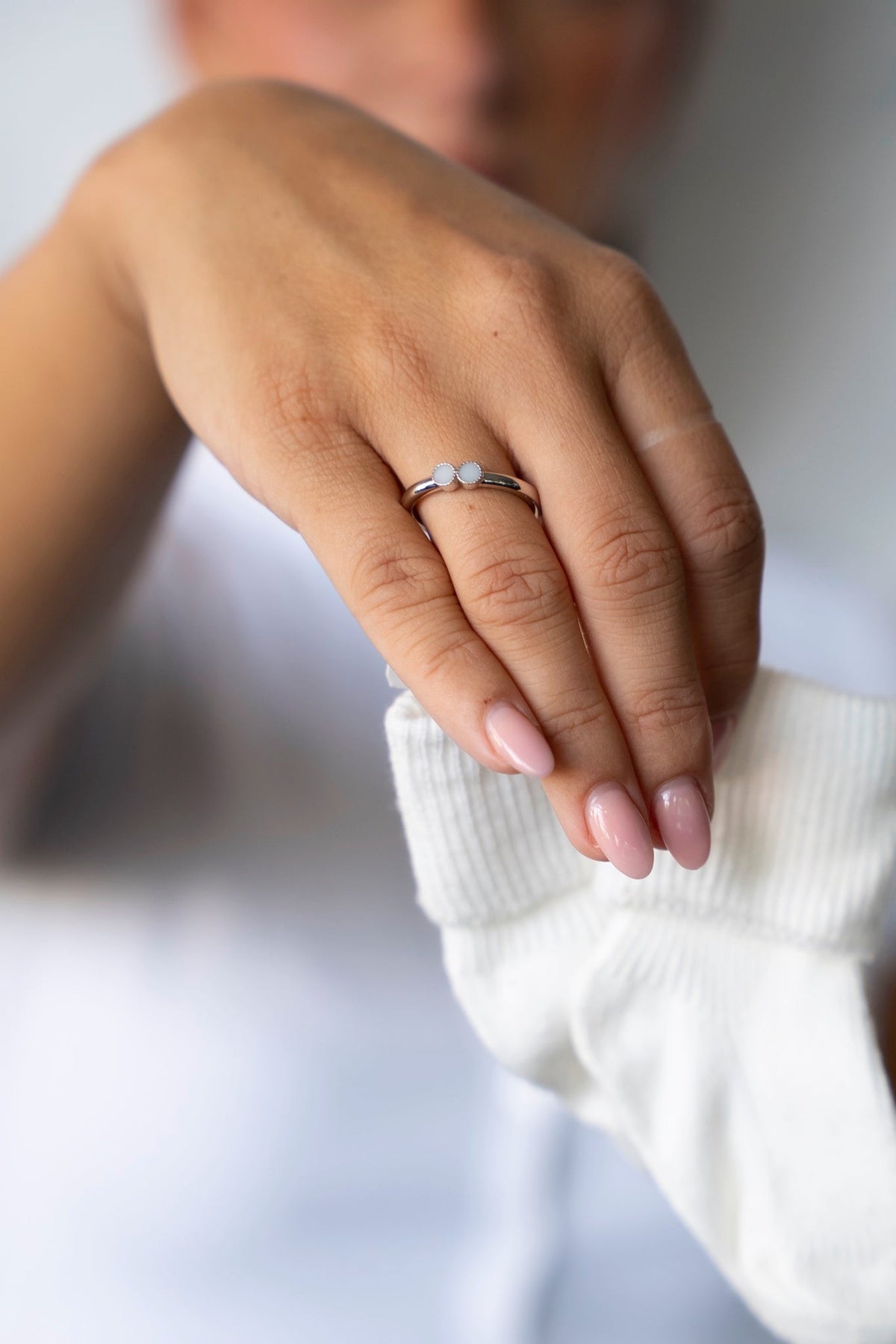 Main portant la bague au lait maternel Bo en or blanc, tenant une chaussette de bébé blanche.