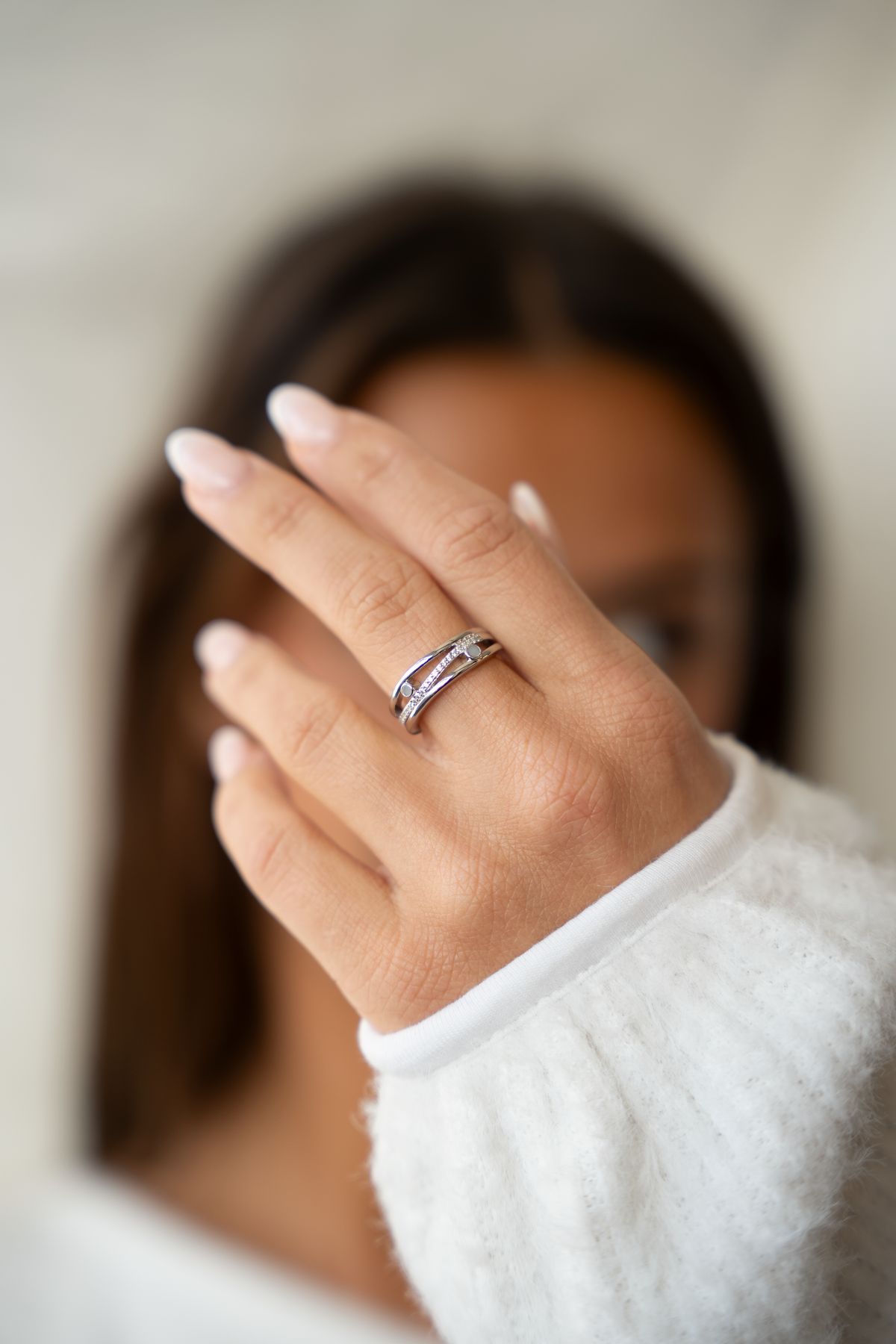 Main devant le visage, pull blanc moelleux, portant la bague Charlotte argentée à trois anneaux