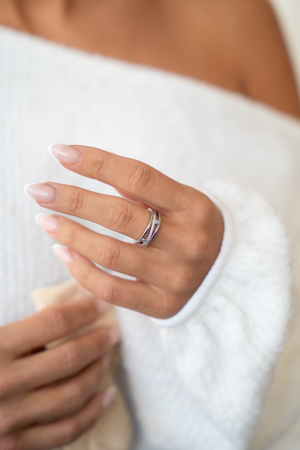 Main posée sur un pull blanc portant la bague Charlotte argentée avec ses deux pierres de lait