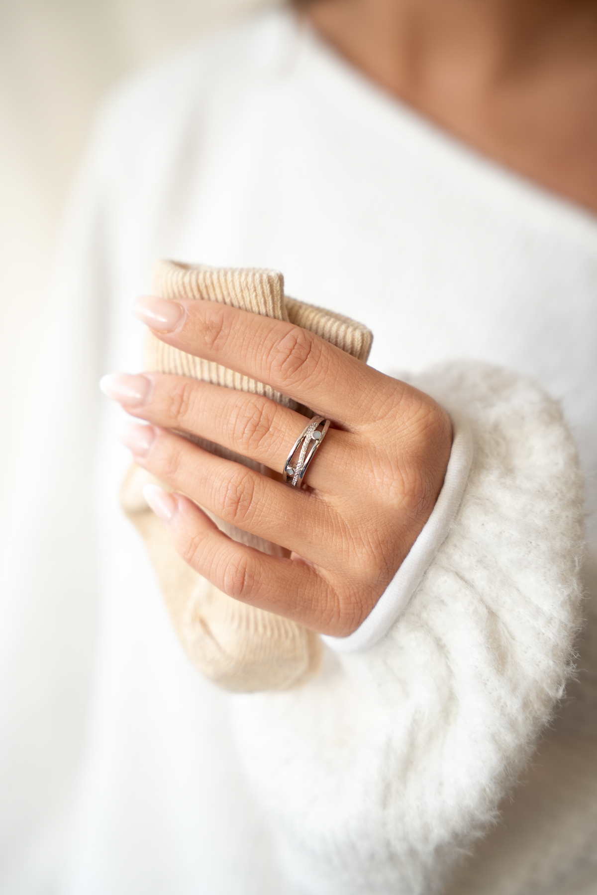 Main tenant des chaussettes de bébé contre un pull blanc, bague Charlotte argentée au doigt