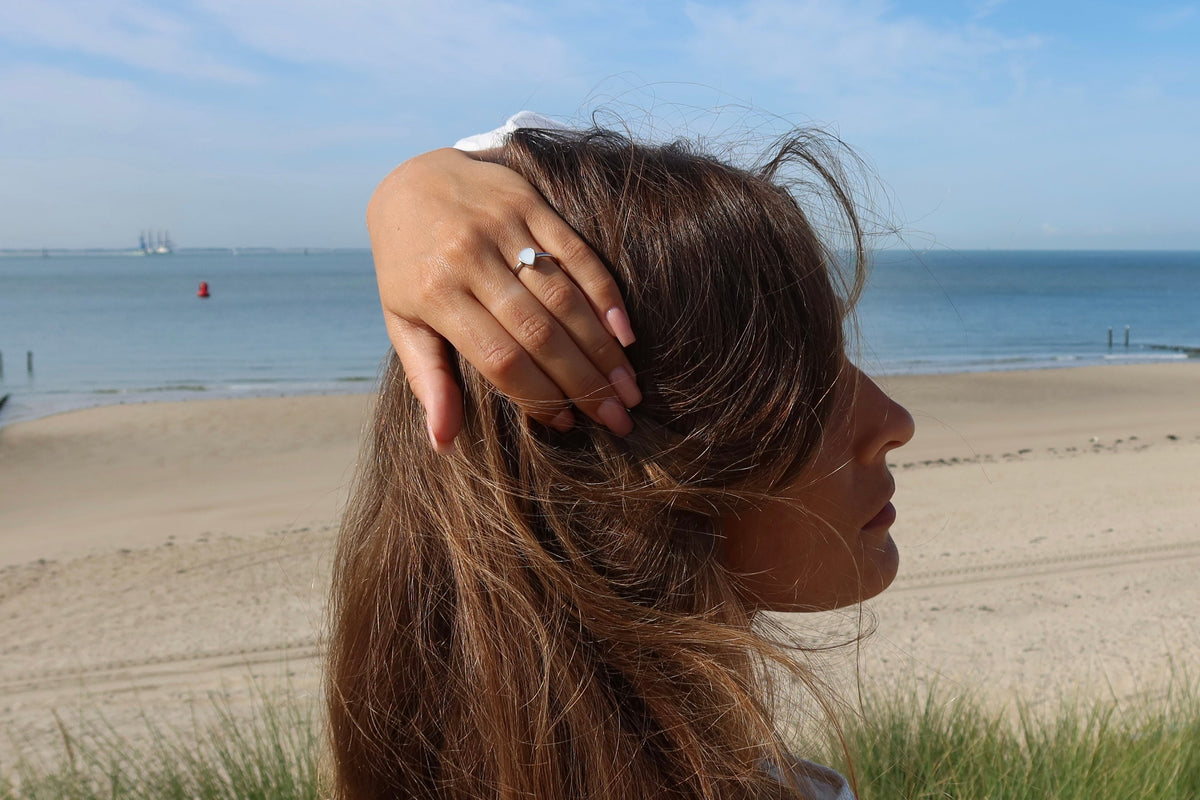 Femme de profil sur la plage, main sur la tête, portant la bague Droplet argentée