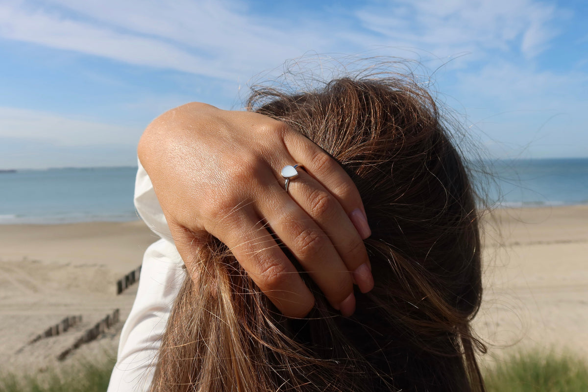 Main dans les cheveux face à la mer, portant la bague Droplet argentée en forme de goutte