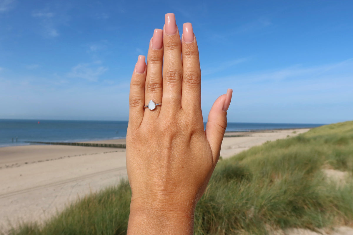 Dos de la main levée devant la plage et les dunes, bague Droplet argentée en goutte