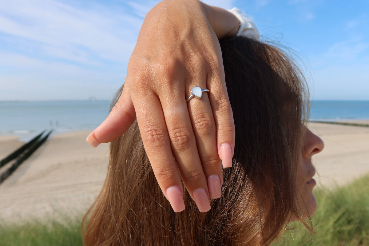 Gros plan d'une main posée sur la tête face à la plage, bague Droplet argentée