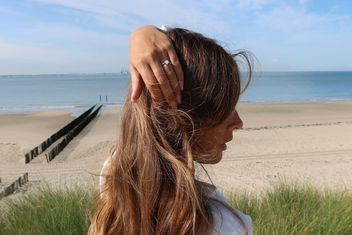 Femme de profil sur la plage, main dans les cheveux, portant la bague Droplet argentée