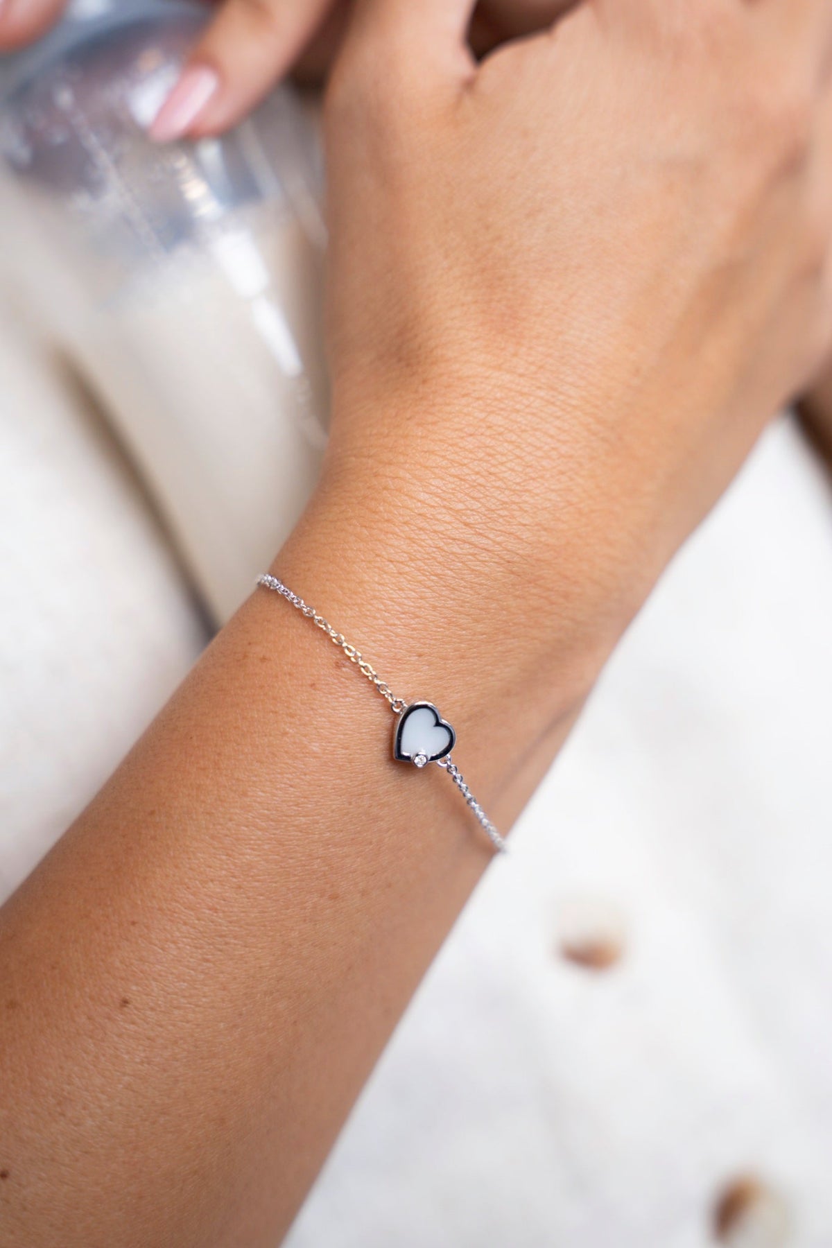 Bracelet Esmée en argent avec pierre de lait maternel en forme de cœur au poignet, à côté d'un biberon de lait.