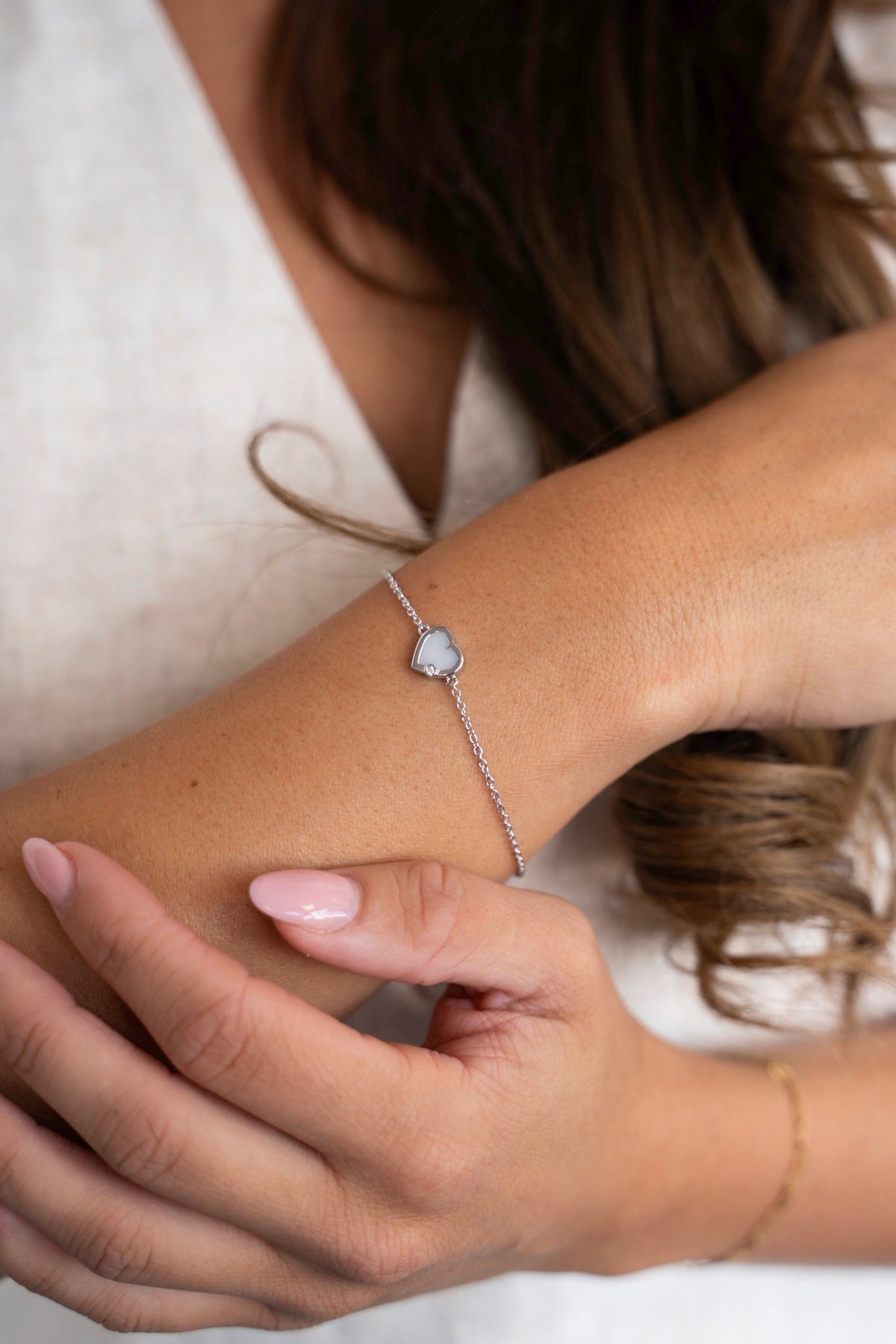 Bracelet Esmée en argent 925 avec cœur de lait maternel, porté au poignet devant un haut en lin.