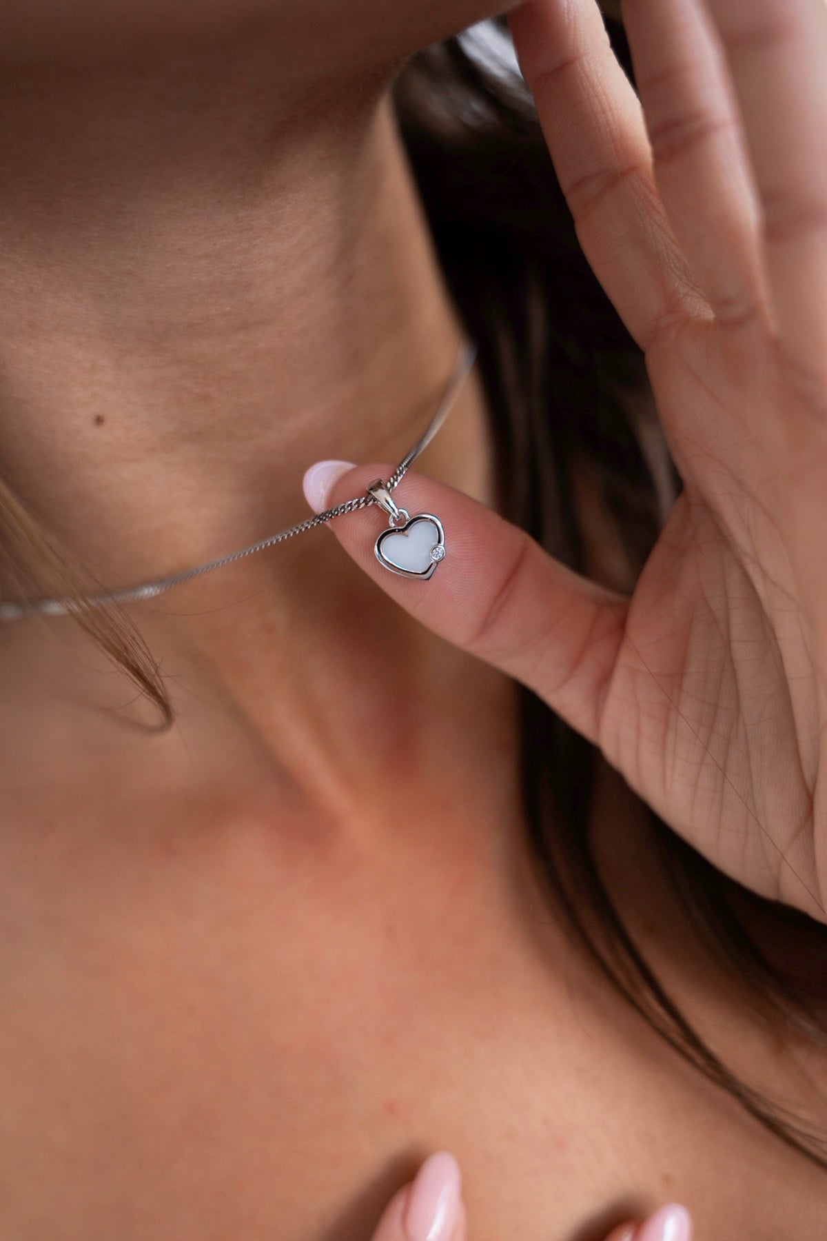 Des doigts tiennent le pendentif Esmée en or blanc en forme de cœur, avec lait maternel et une petite pierre.