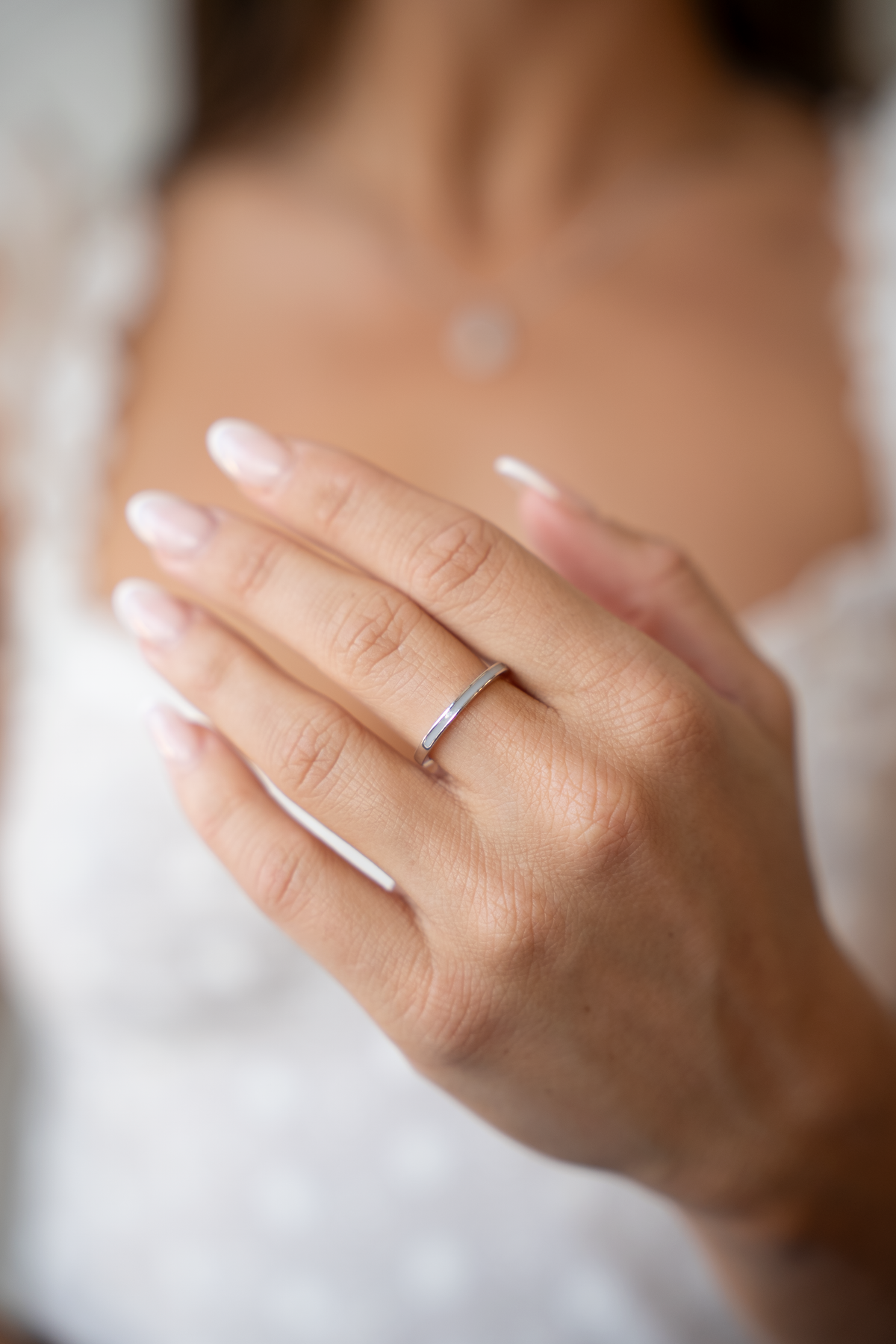Gros plan d'une main portant la bague Eva en argent devant un haut blanc