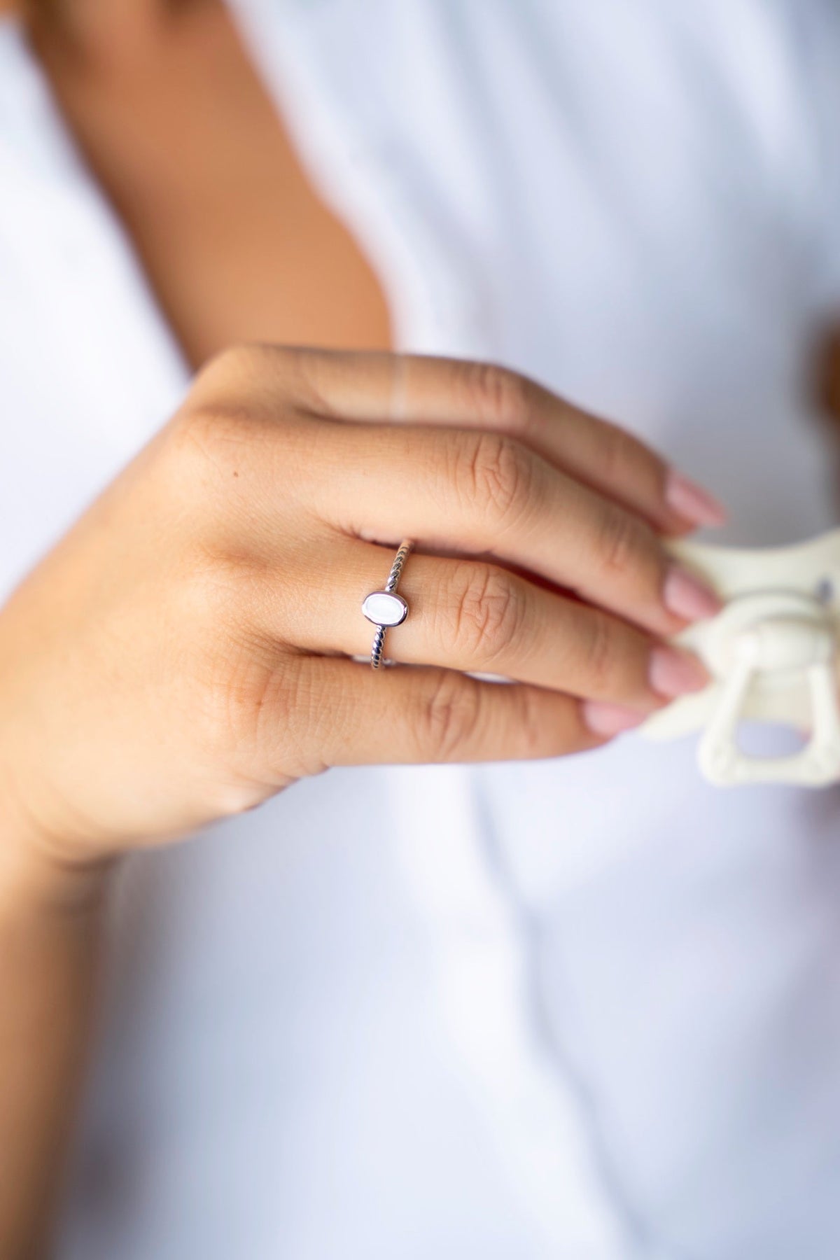 Bague Ilse en or blanc avec pierre ovale de lait maternel et anneau travaillé, une tétine à la main.
