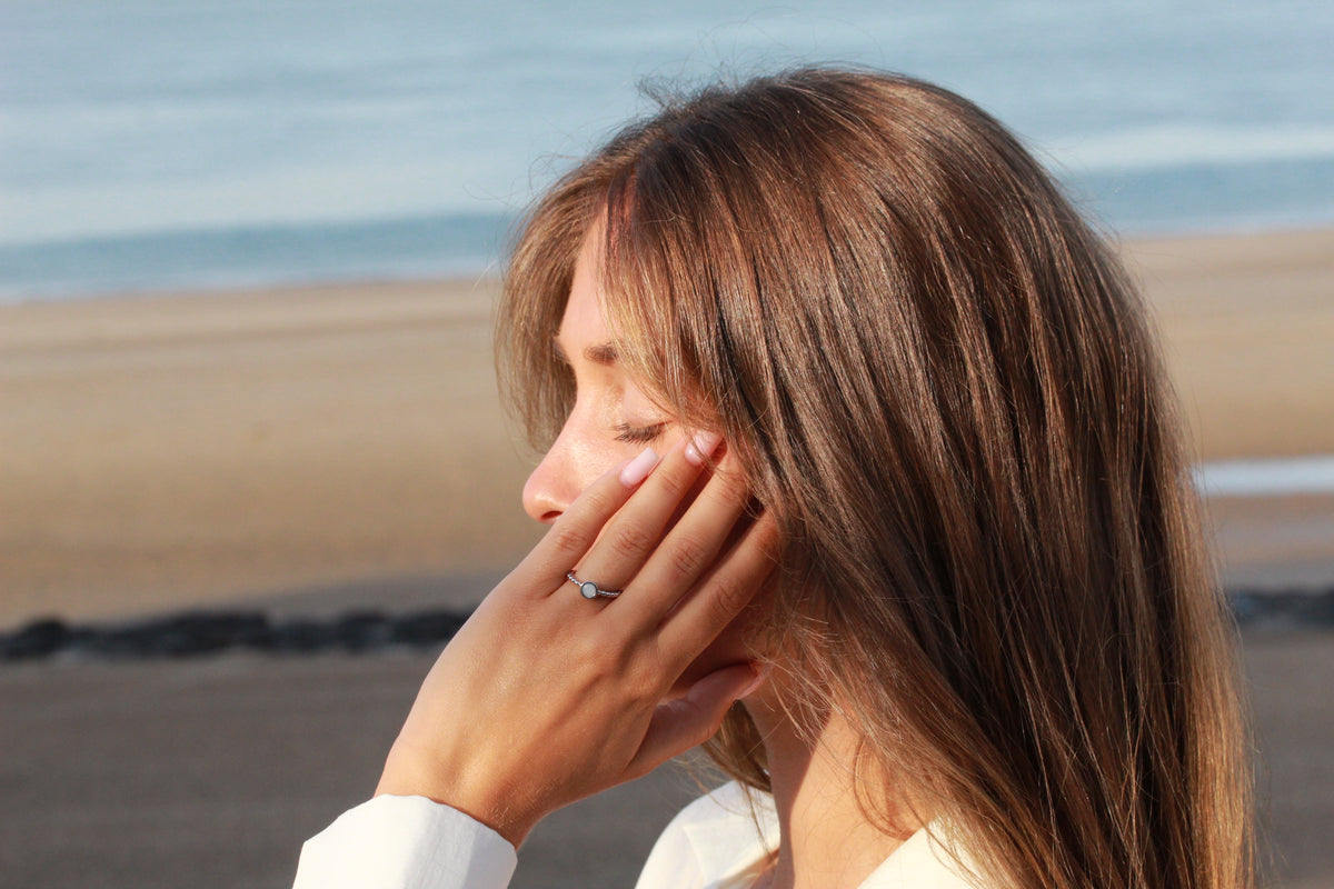 Femme à la plage, main contre la joue avec la bague Isabelle en argent
