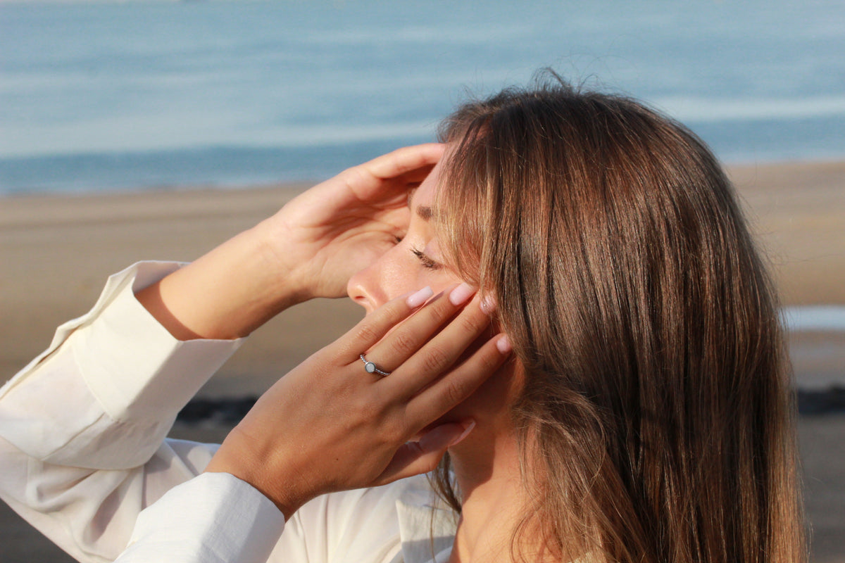 Bague Isabelle en argent portée, mains près du visage, femme en chemise blanche à la plage