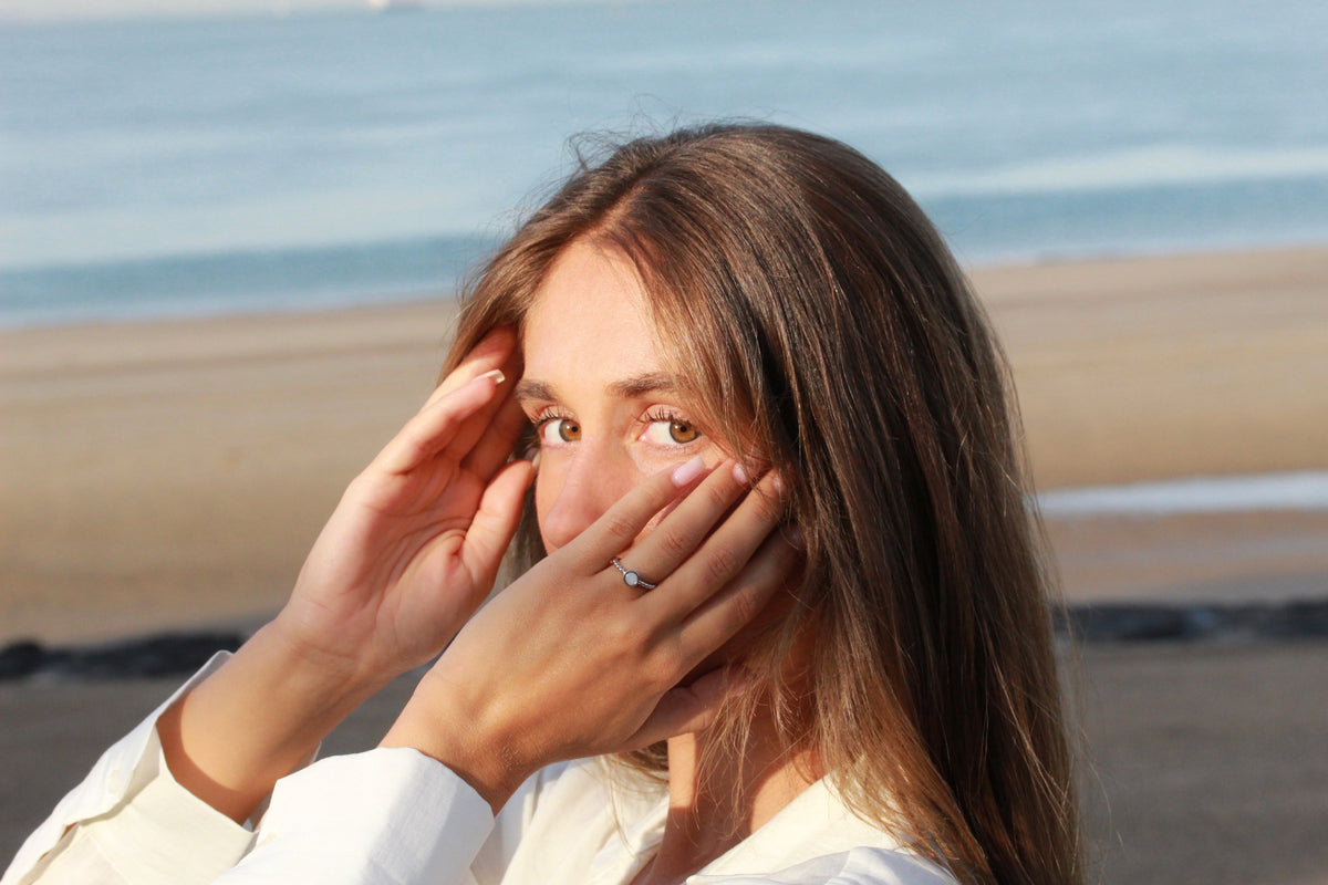 Femme regardant l'objectif, mains près du visage, bague Isabelle en argent au doigt