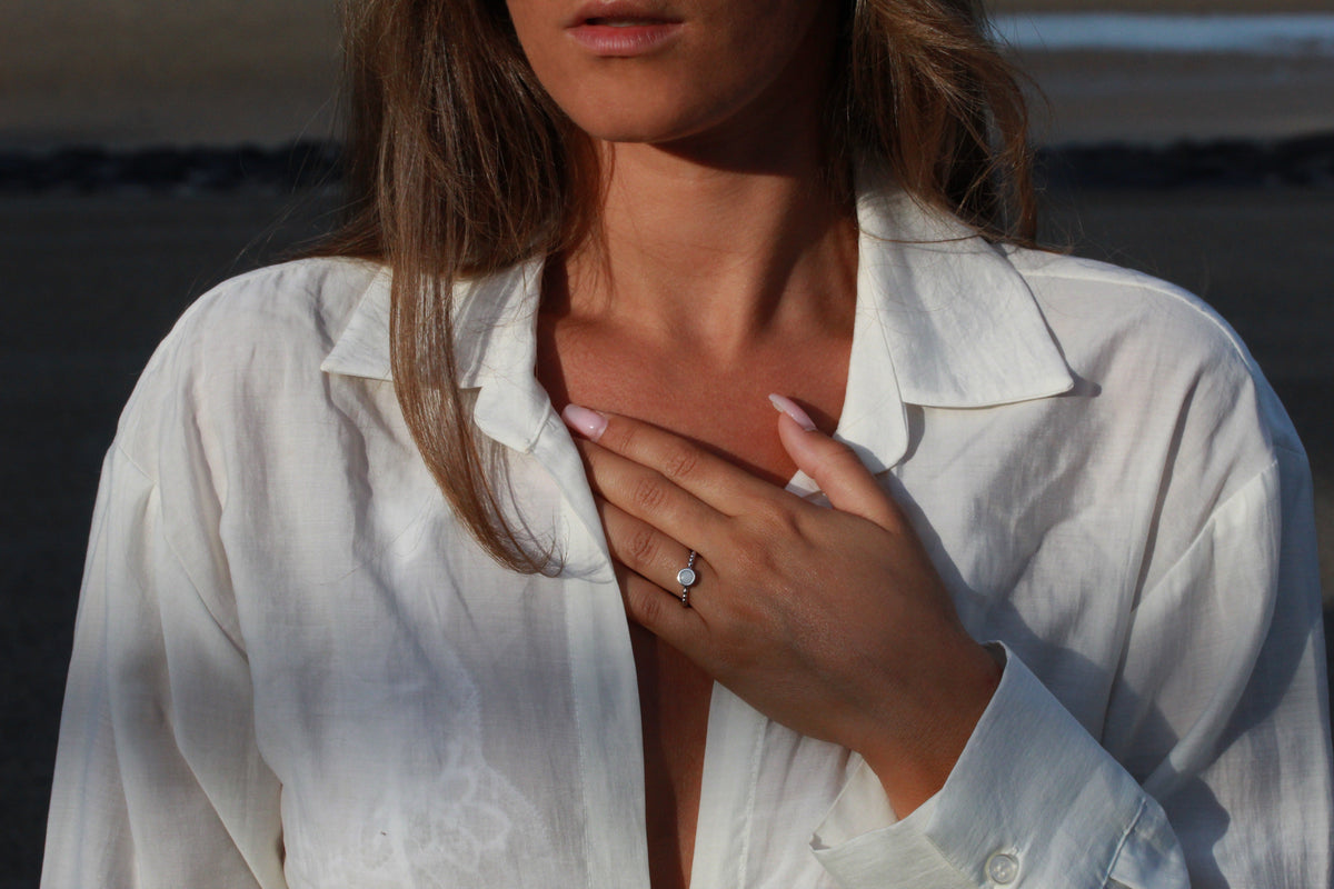 Bague Isabelle en argent portée, main posée sur la poitrine, chemise blanche ouverte