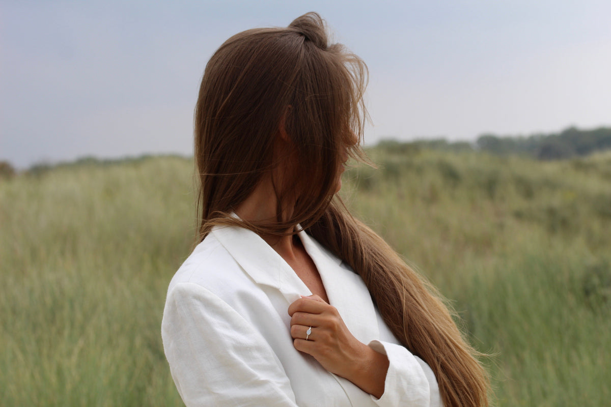 Femme de profil dans les dunes, cheveux au vent, bague Juna en argent au doigt