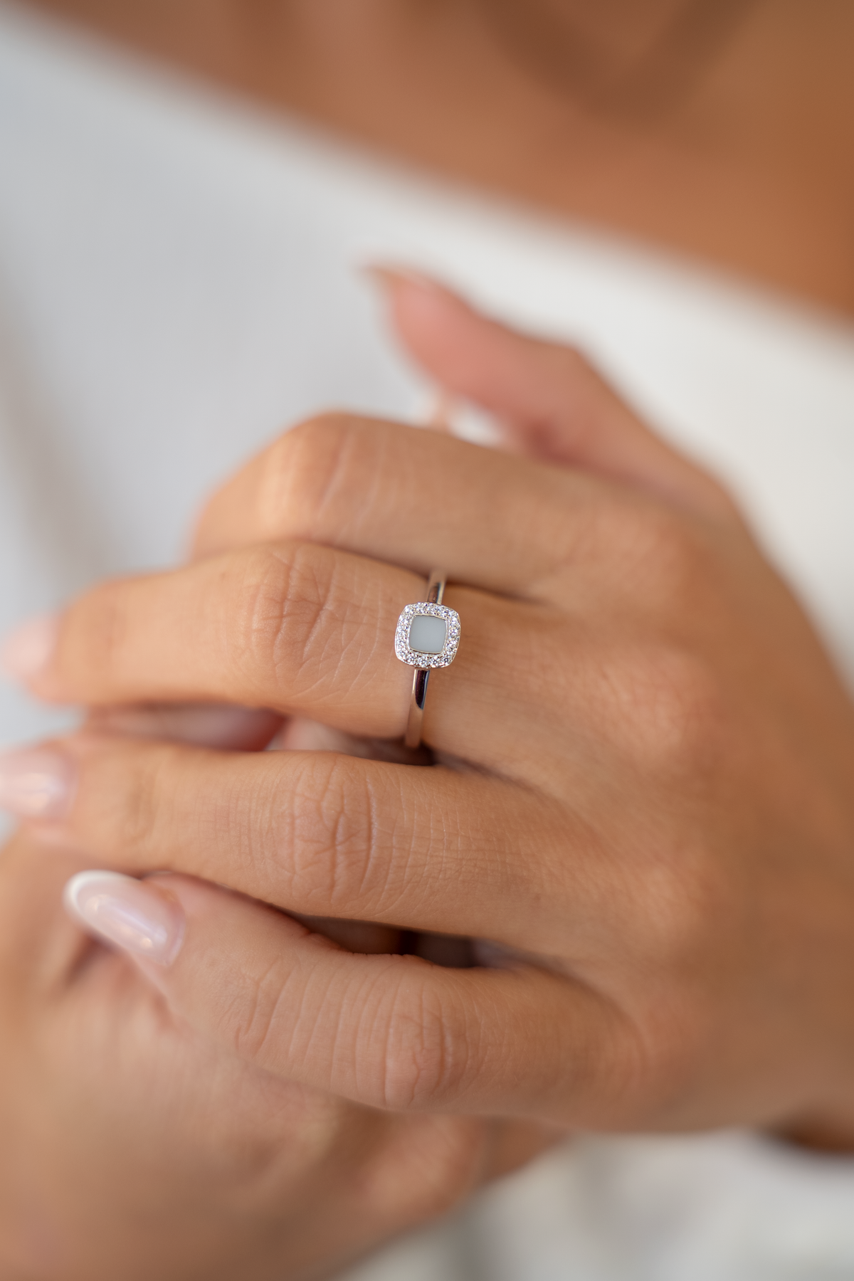 Gros plan de mains jointes portant la bague Lara couleur argent à pierre carrée