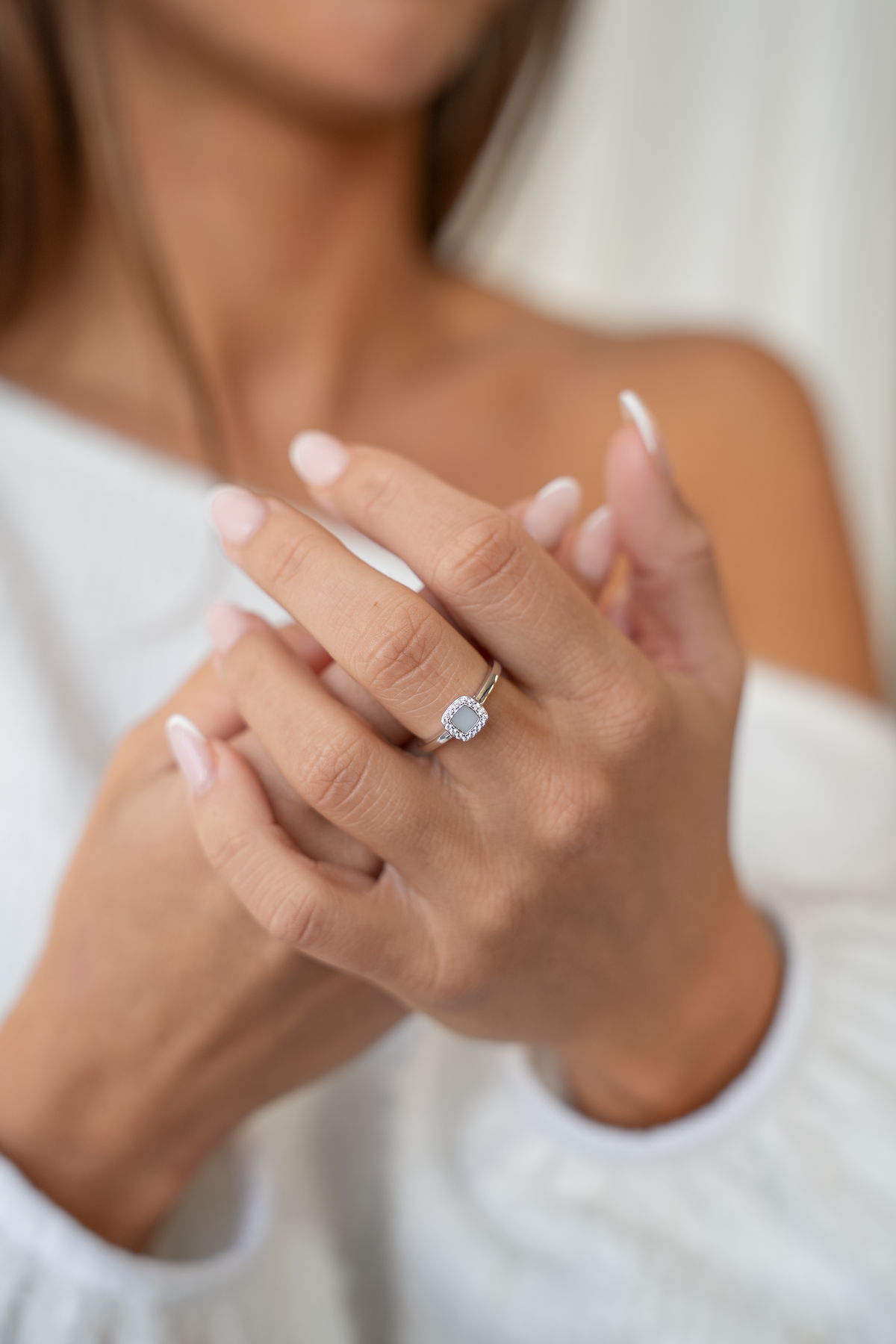 Bague Lara couleur argent portée, mains jointes devant un pull blanc