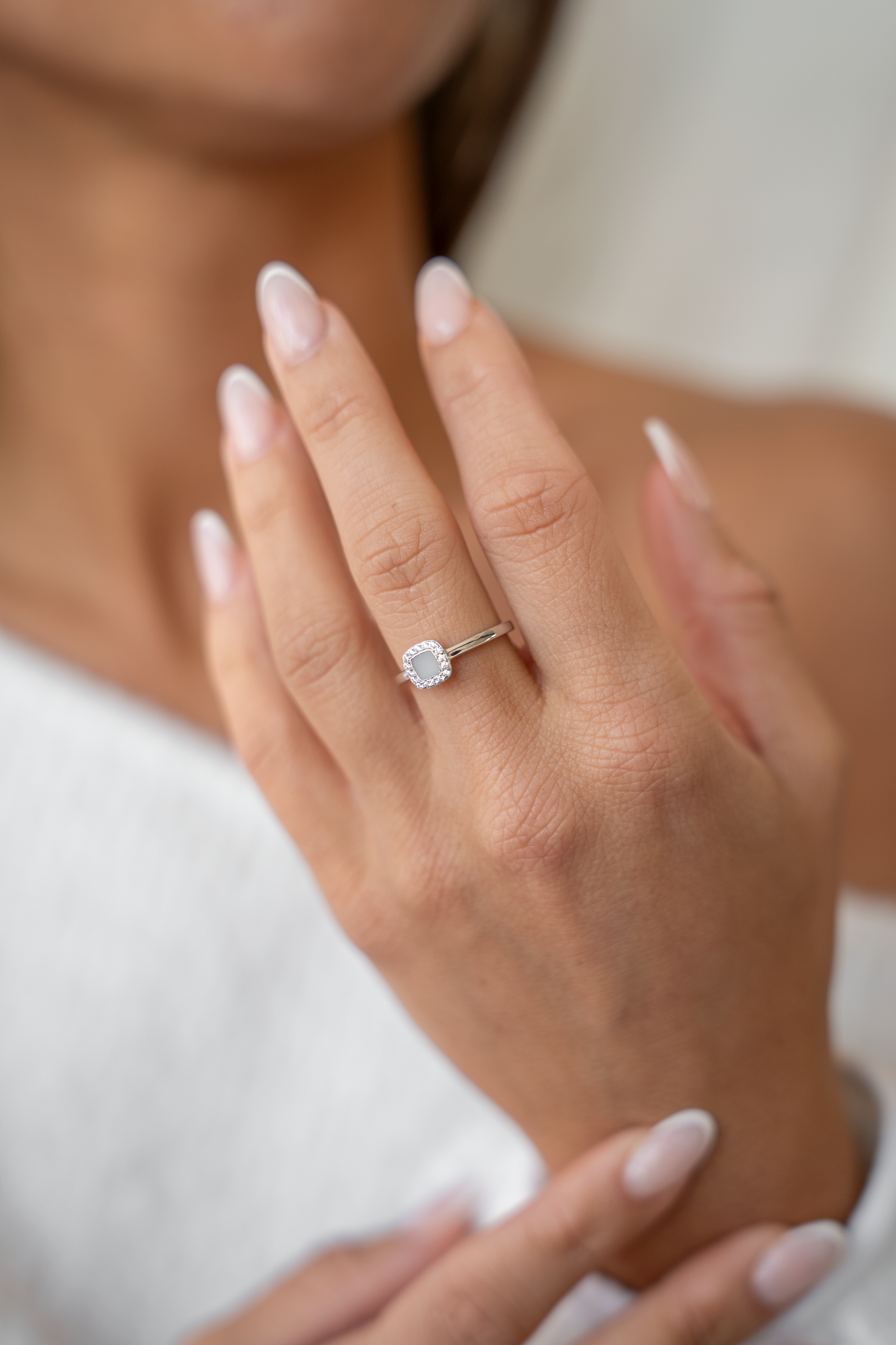 Main près du cou portant la bague Lara couleur argent à pierre carrée entourée