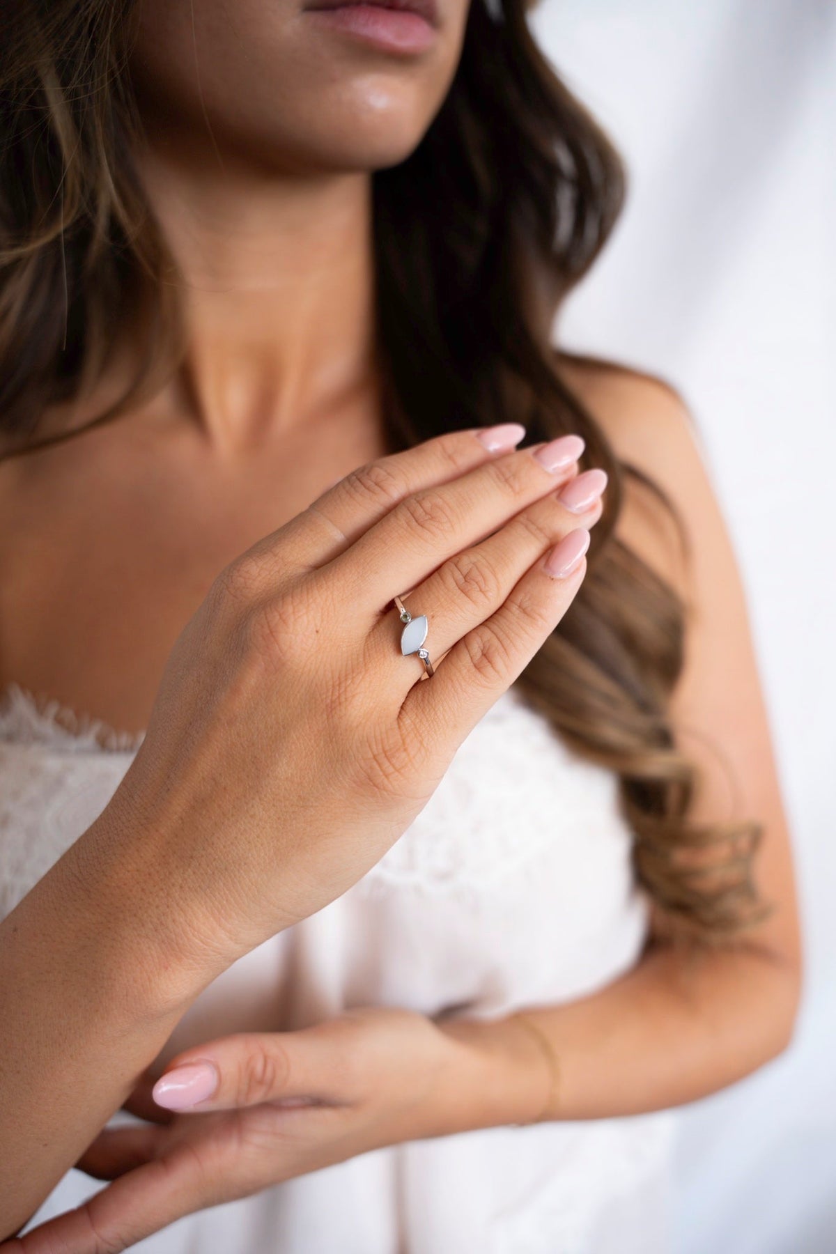 Femme en haut de dentelle blanc portant la bague au lait maternel Lina Duo en or blanc massif à l'annulaire.