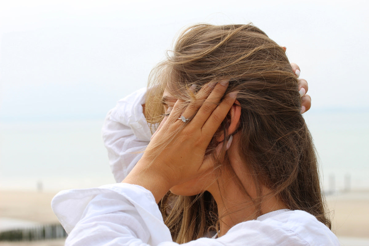 Femme à la plage, main dans les cheveux, bague Lina couleur argent au doigt