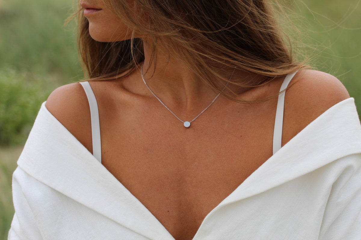Collier Lis en argent porté sur le décolleté, petite pierre ronde de lait maternel sur fine chaîne