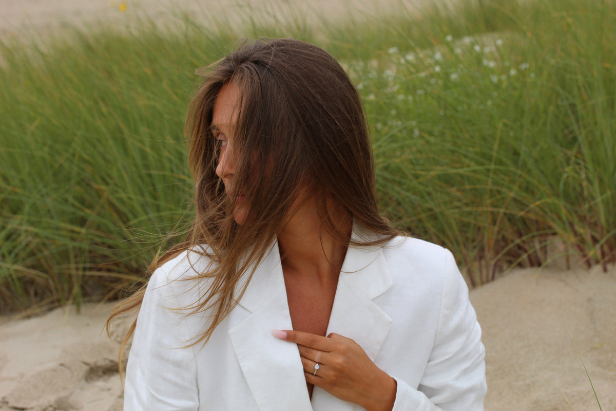 Femme dans les dunes en blazer blanc, bague Lis couleur argent à la main