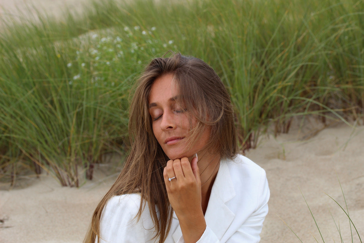 Femme les yeux fermés dans les dunes, main sous le menton avec la bague Lis couleur argent