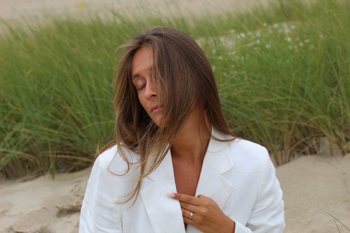 Bague Lis couleur argent portée, main sur la poitrine, femme en blazer blanc dans les dunes
