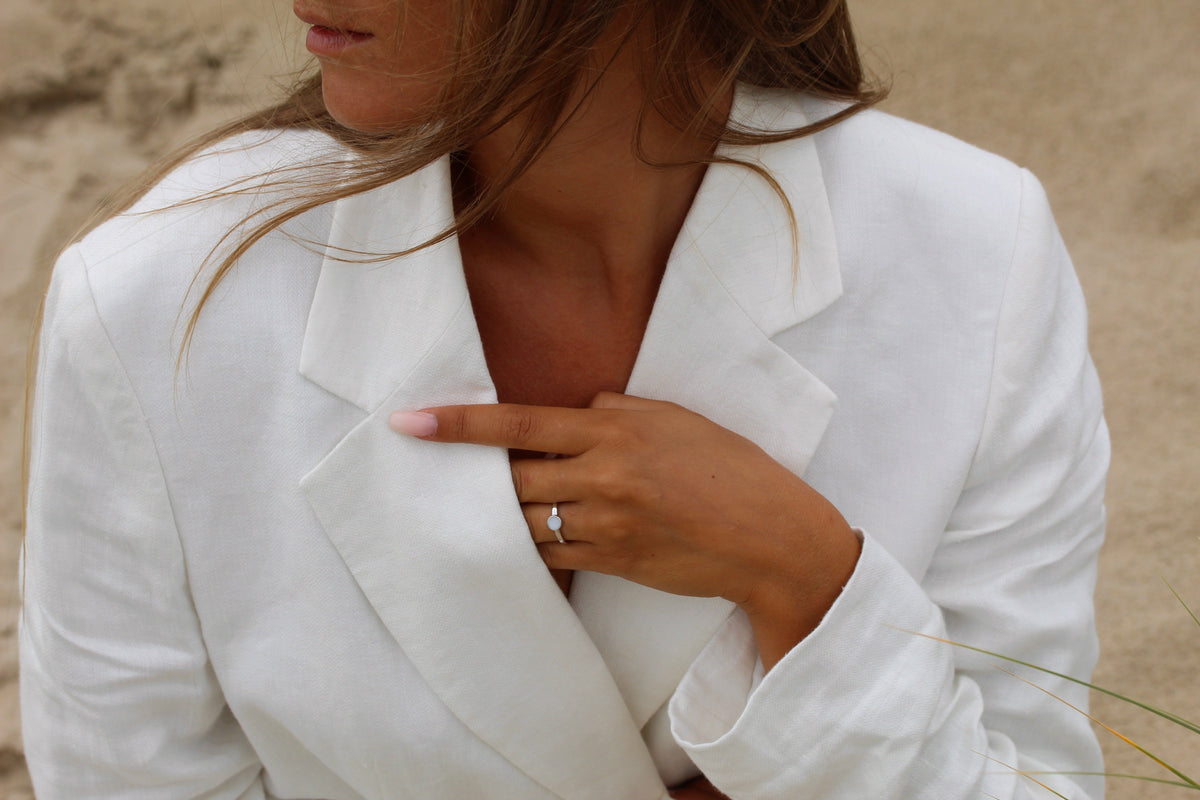 Bague Lis couleur argent portée, main posée sur un blazer en lin blanc