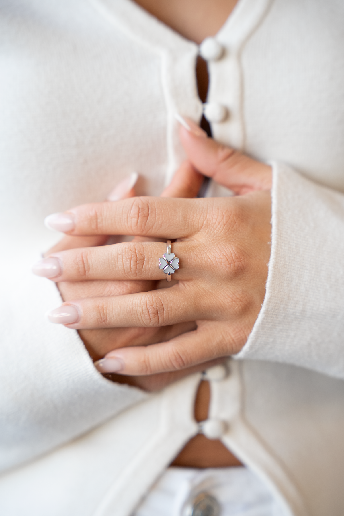 Bague trèfle Lucy en argent portée à l'annulaire, mains jointes sur un gilet blanc