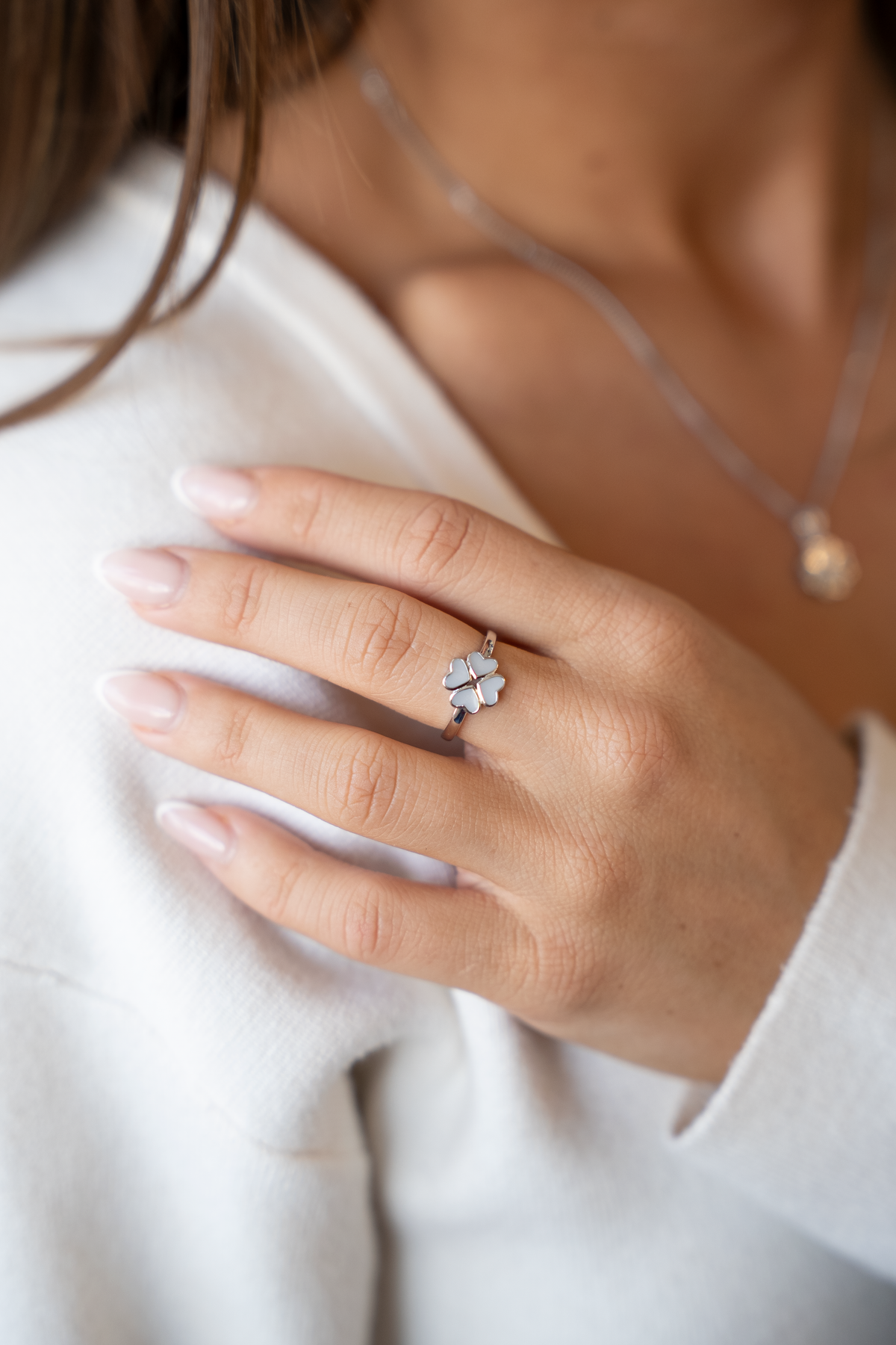 Main posée sur l'épaule portant la bague trèfle Lucy couleur argent à quatre cœurs de lait