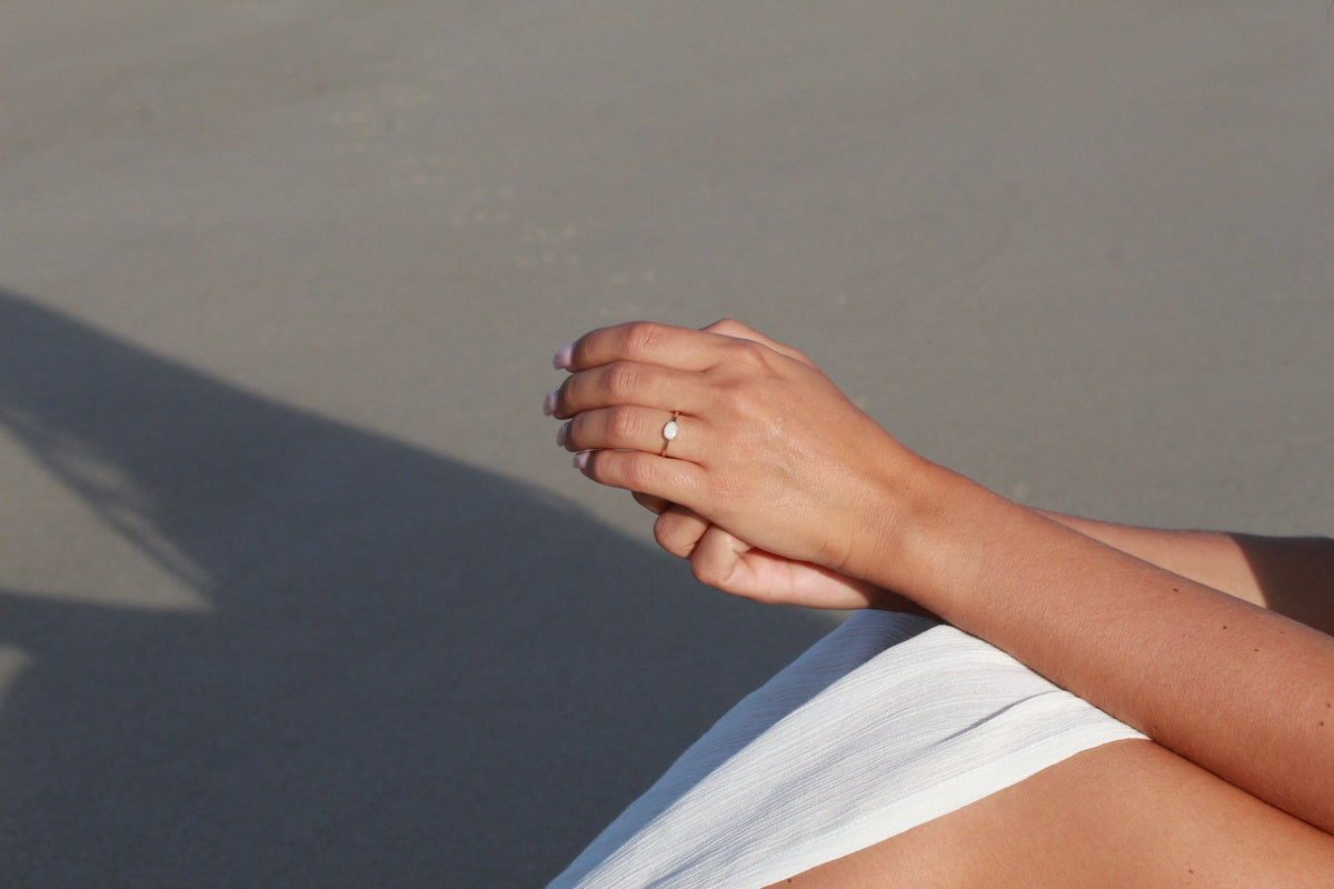 Mains jointes sur la plage, bague Luna avec petite pierre ovale de lait maternel portée au doigt