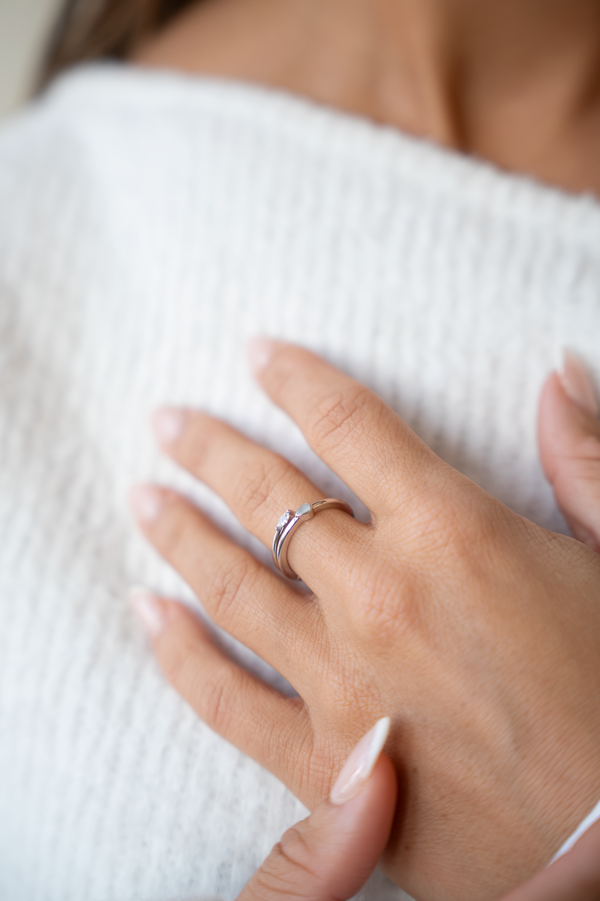 Main sur un pull blanc portant la bague ouverte Naomi couleur argent avec goutte de lait maternel