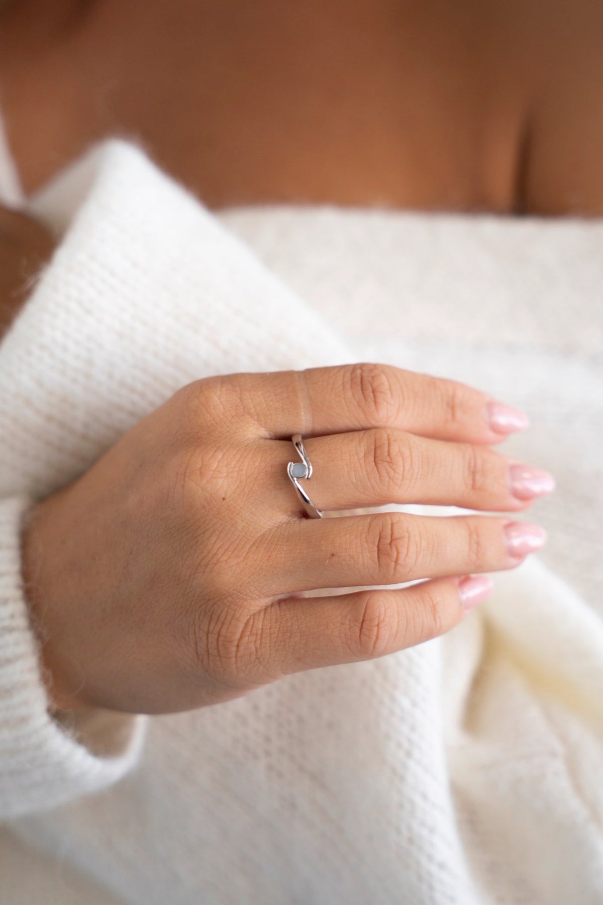 Bague Olivia en or blanc avec une petite pierre de lait maternel, la main sur un pull blanc.